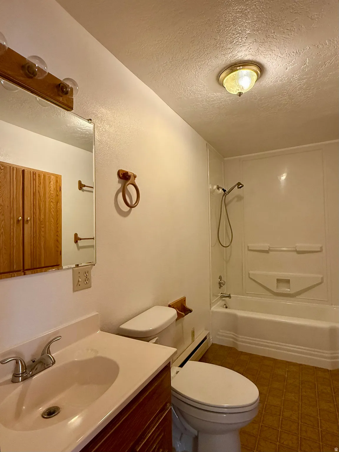 Bathroom featuring a white vanity with integrated sink, wood-finish cabinetry, mirrored wall, toilet, and a bathtub with a shower kit