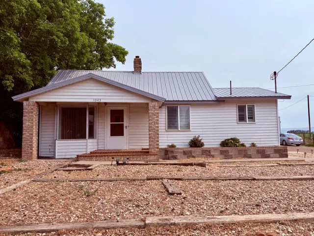 White siding residence featuring a corrugated metal roof, brick columns, a covered porch, and a brick chimney