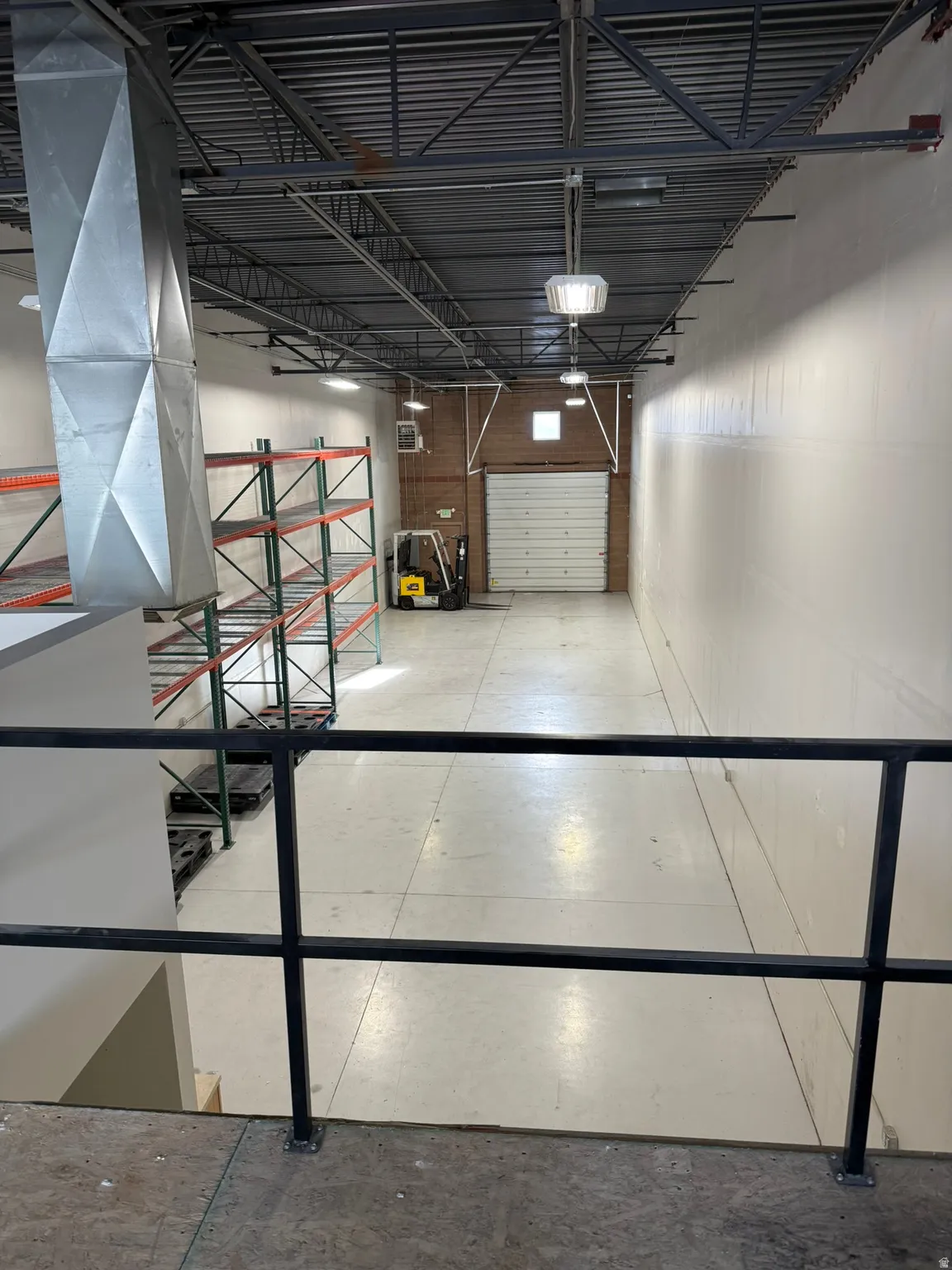 Industrial interior featuring a metal ceiling, exposed ductwork, concrete flooring, and suspended lighting fixtures