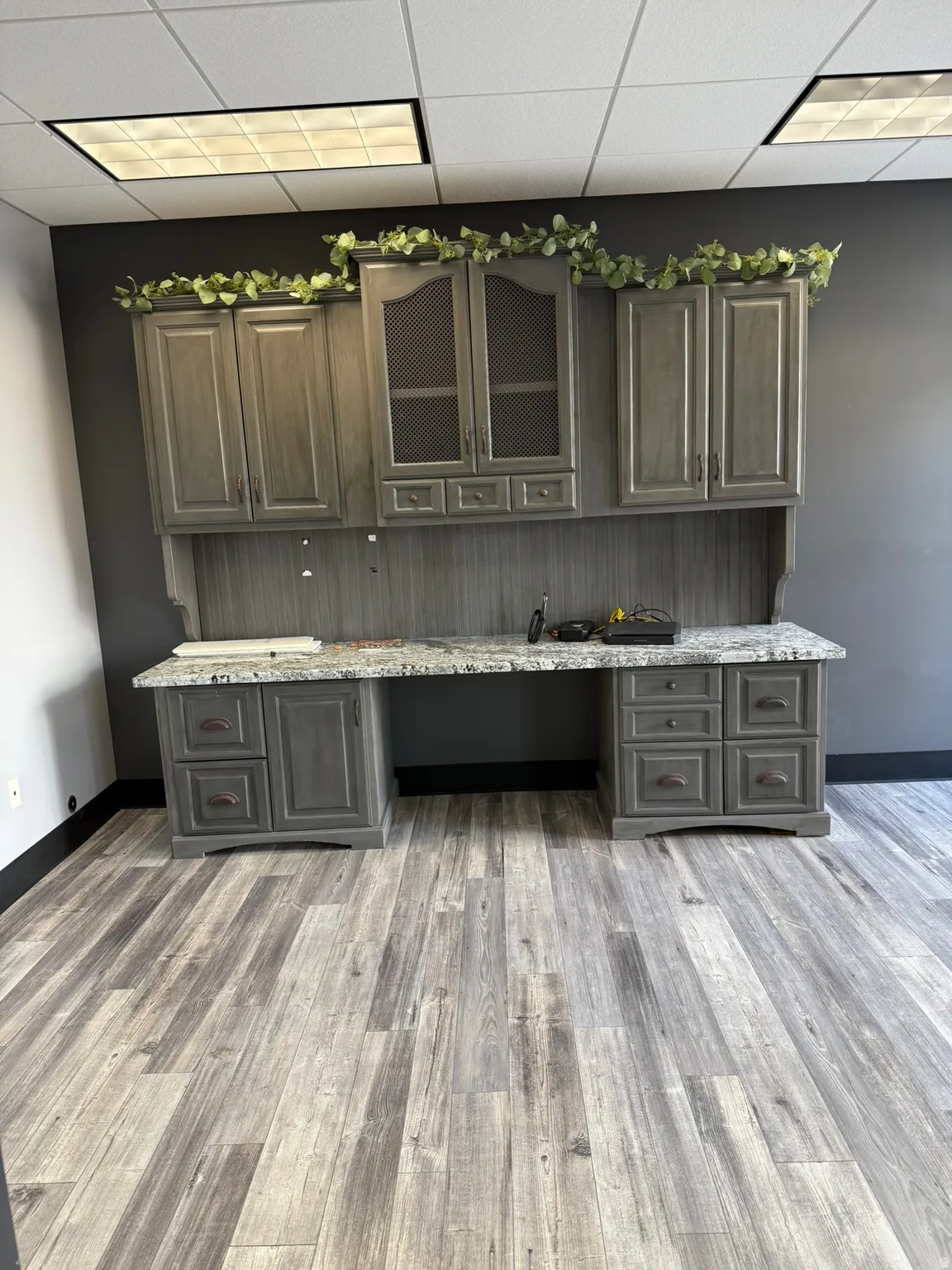 Integrated built-in desk unit featuring gray cabinetry, a speckled countertop, and wood-finish flooring