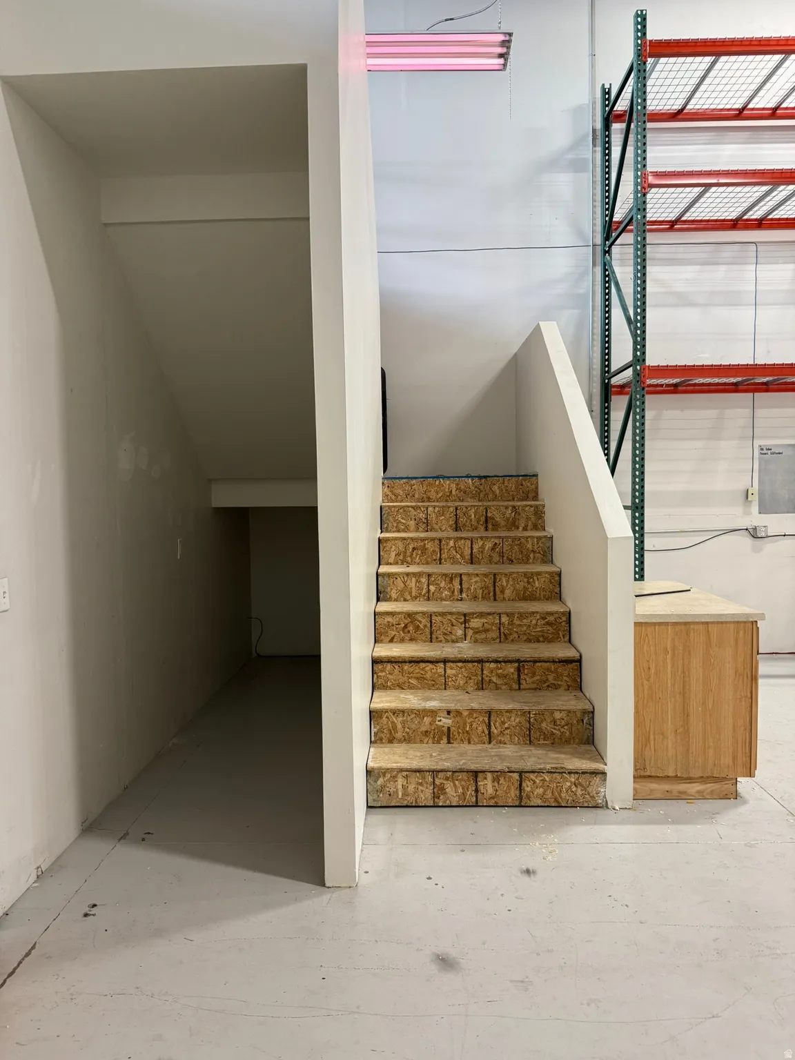 Stairwell with unfinished wood steps, white painted walls, and a built-in wood-finish cabinet