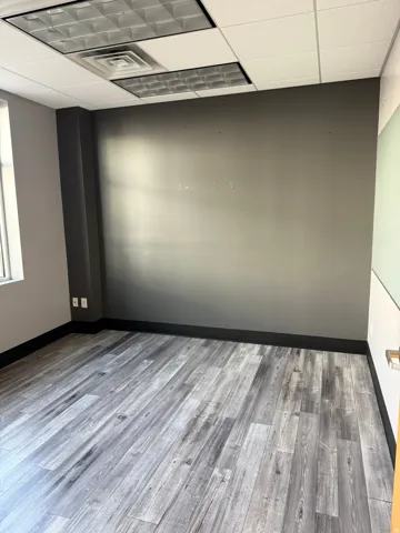 Room featuring wood-finish flooring, dark gray accent wall, and drop ceiling with integrated lighting