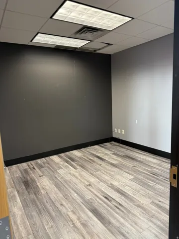 Room featuring wood-finish flooring, dark accent wall, suspended ceiling with recessed lighting, and black baseboards