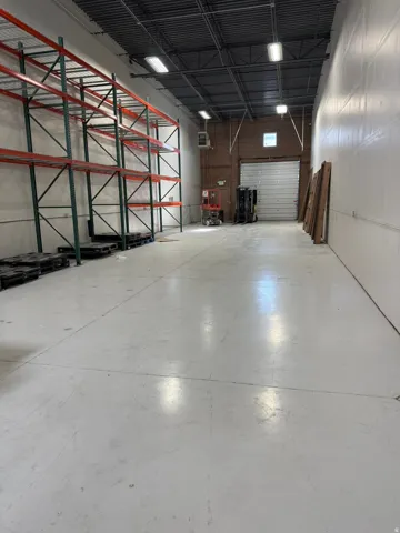 Spacious warehouse interior featuring high ceilings with exposed joists, concrete flooring, and a large roll-up door