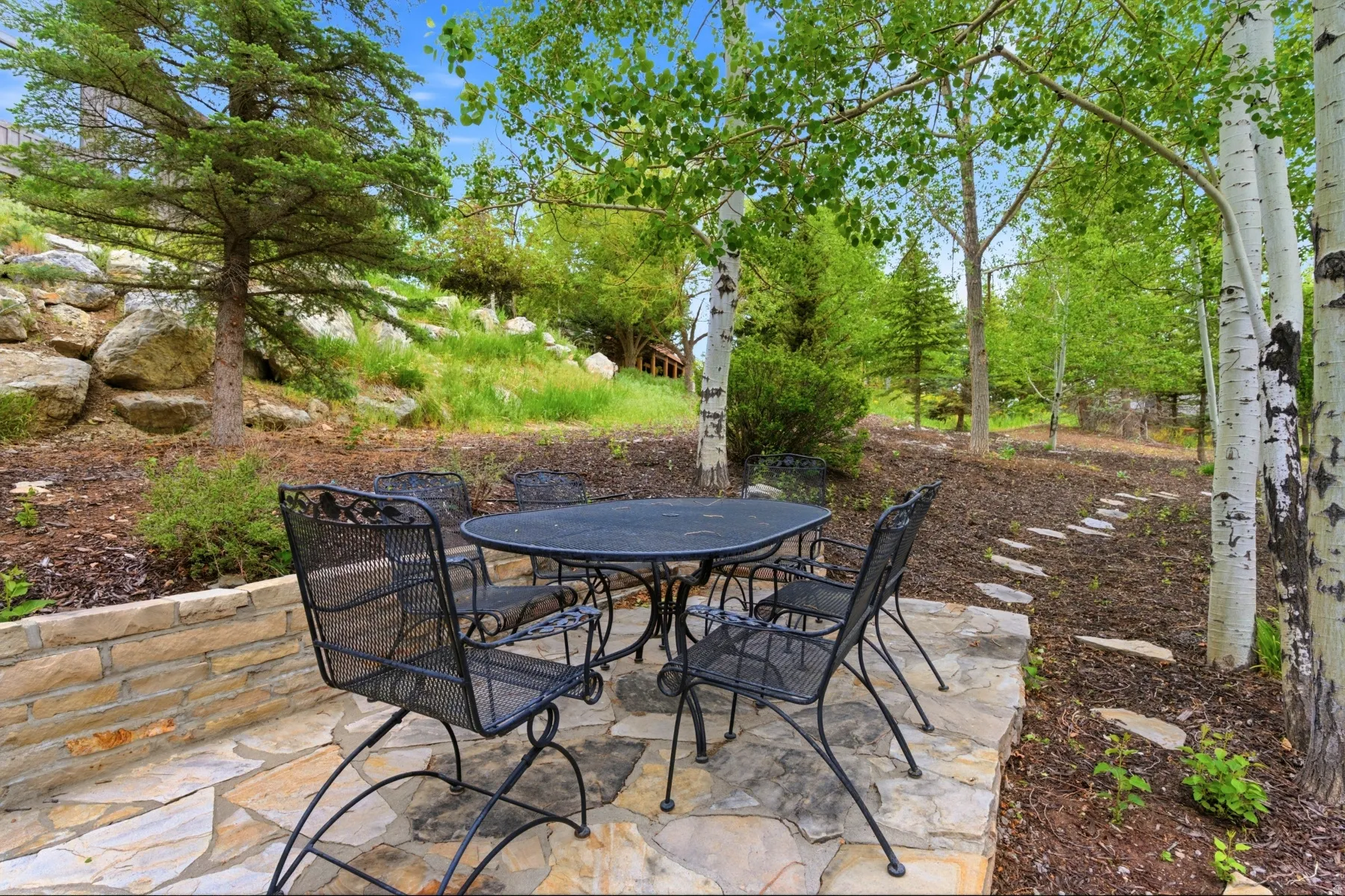 Expansive flagstone patio area with a stone retaining wall and mature landscaping
