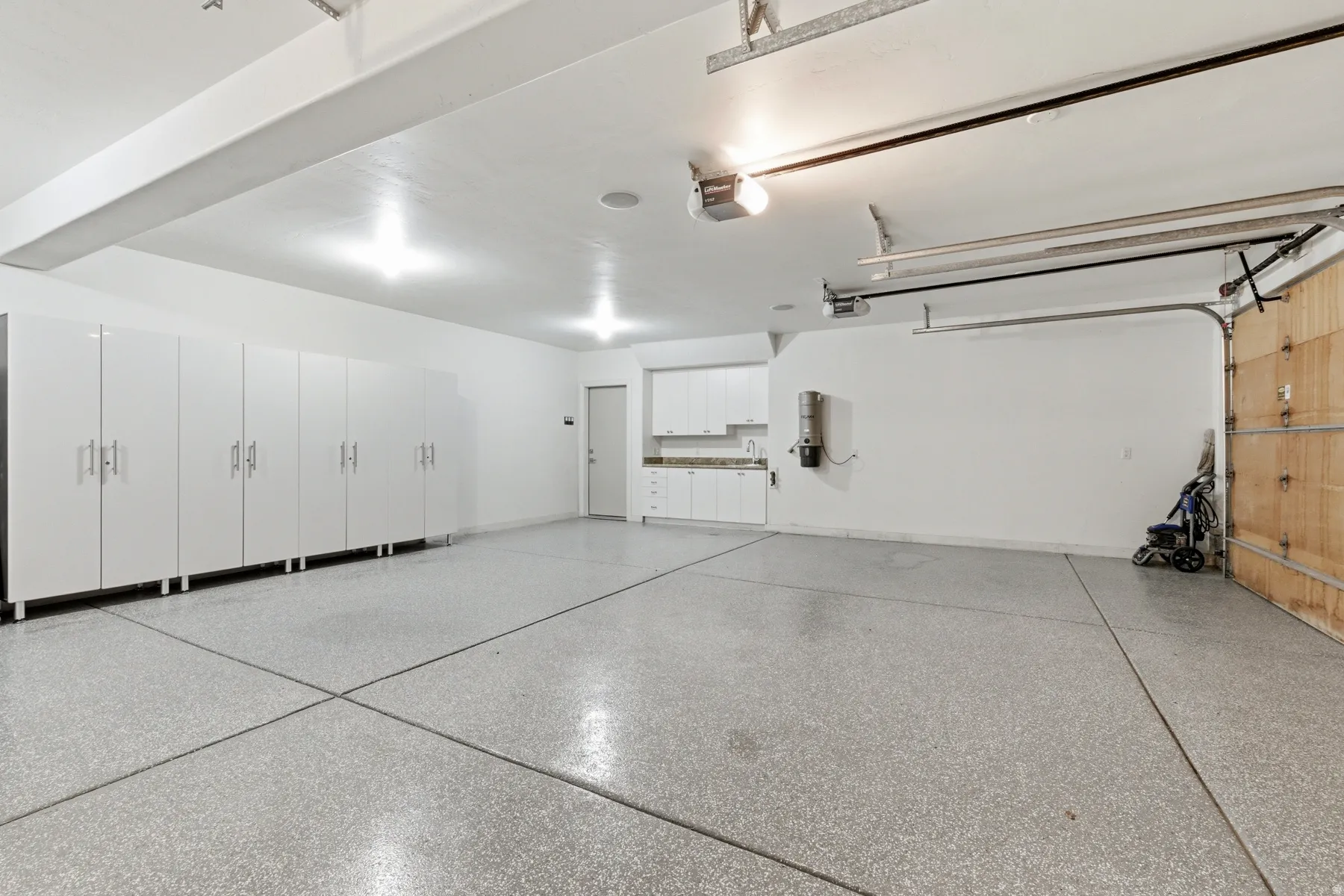 Spacious garage featuring an epoxy-coated concrete floor, extensive white cabinetry with brushed nickel hardware, recessed lighting, and a utility sink area with additional storage