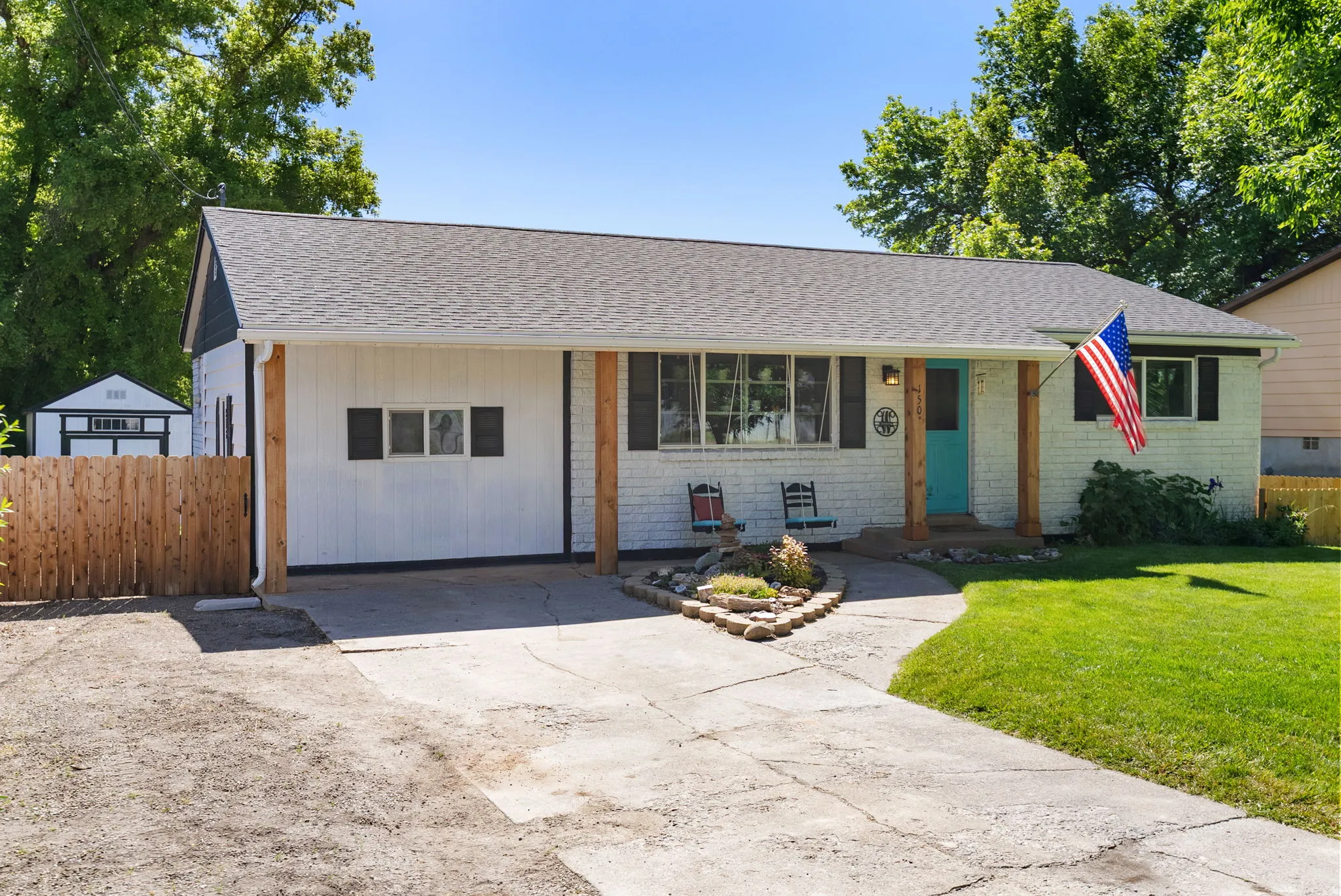 Ranch-style exterior featuring white siding with dark trim, a covered entry with exposed wood posts, and a teal front door
