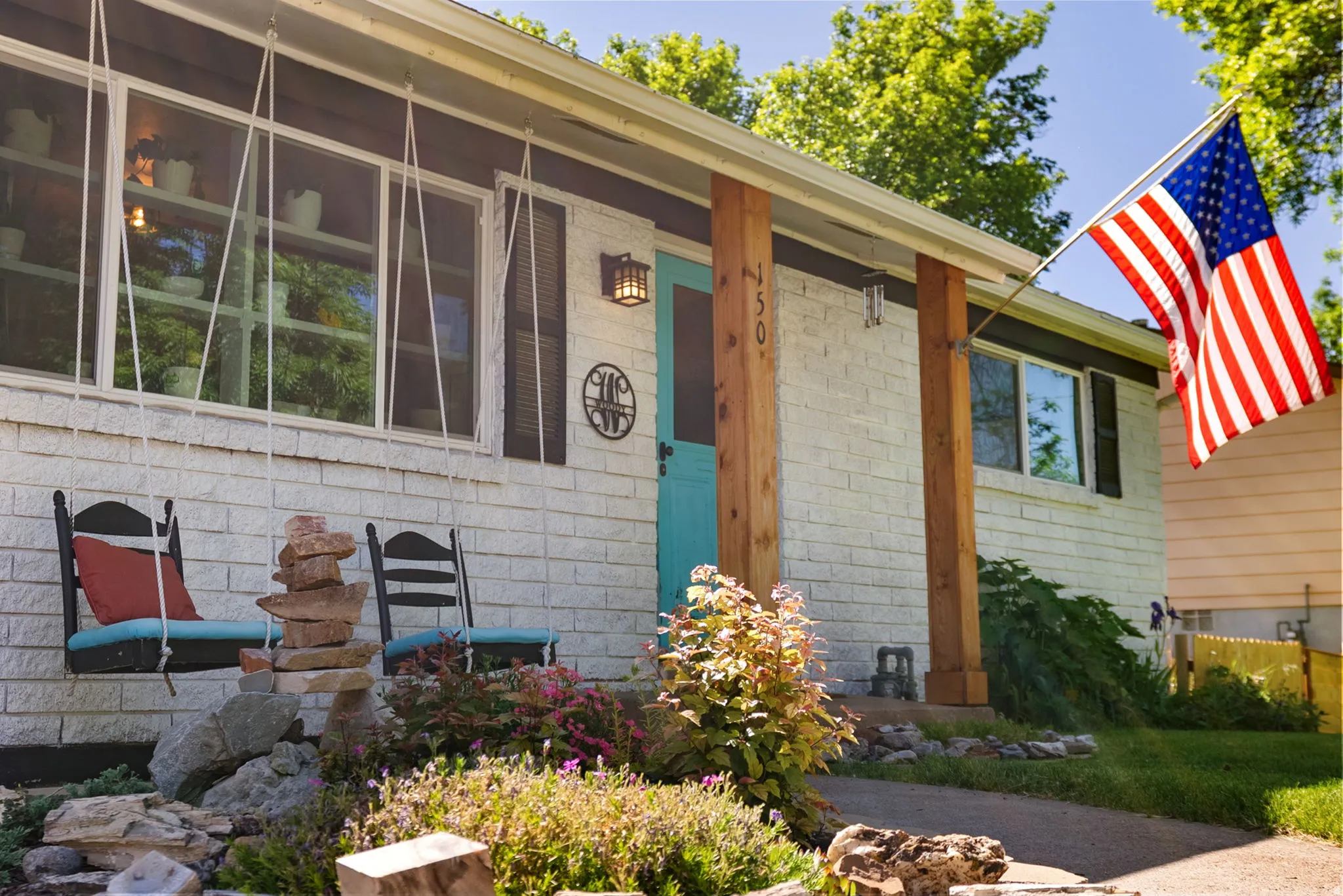 White brick exterior with a vibrant turquoise door, accented by natural wood columns and dark shutters