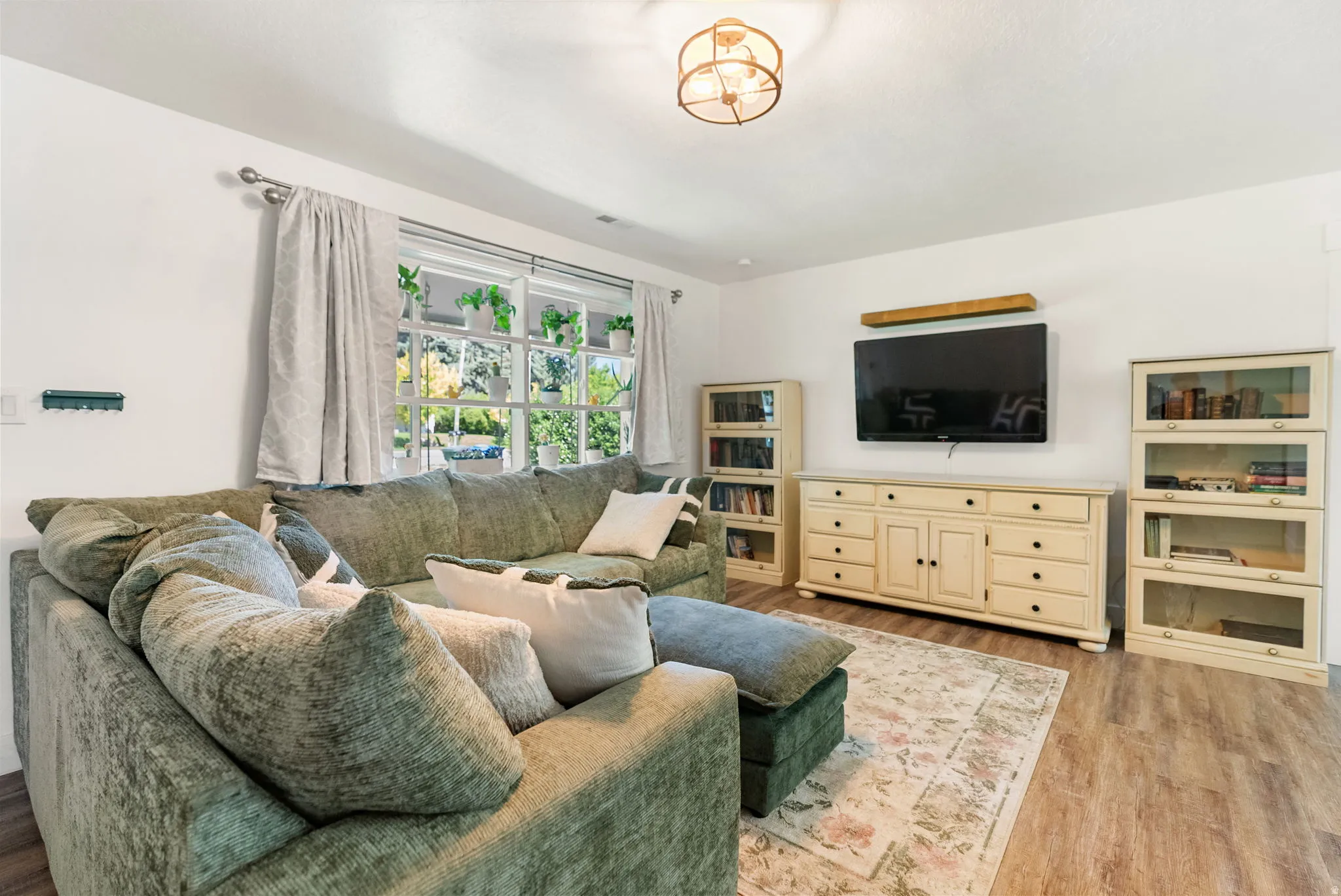 Spacious living area featuring wood-finish flooring, ample natural light from multiple windows, a ceiling-mounted light fixture, and a built-in media console with additional shelving