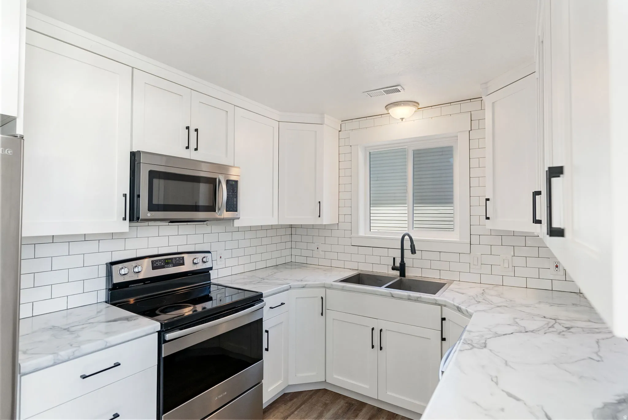 Modern kitchen featuring white shaker cabinetry, stainless steel appliances, marble-look countertops, subway tile backsplash, and wood-finish flooring