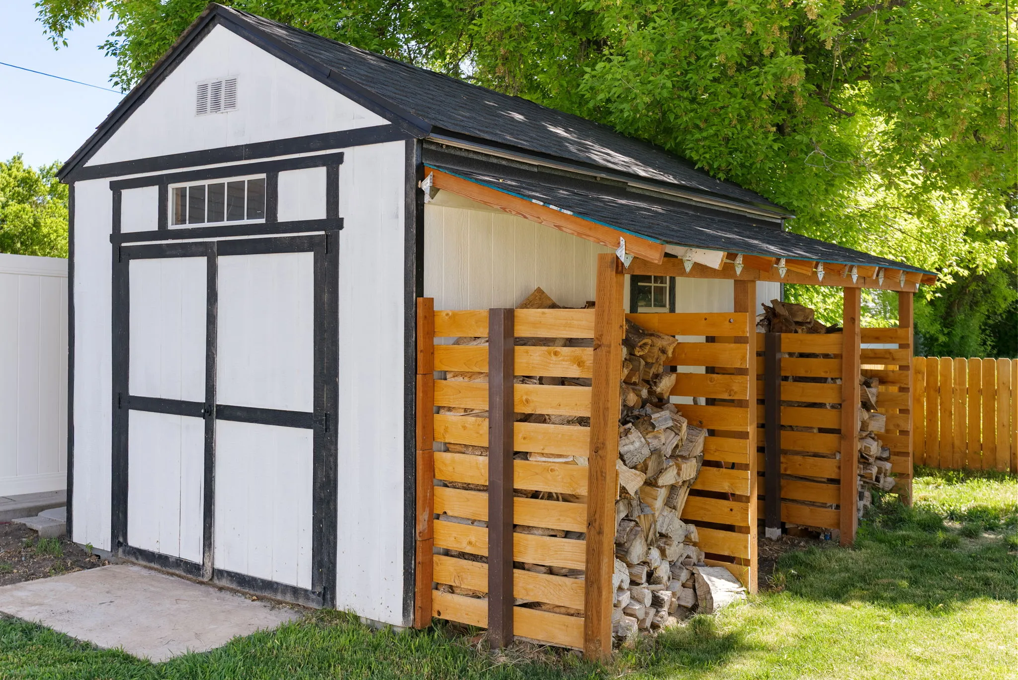 Detached storage shed with a black shingle roof, white siding, and black trim