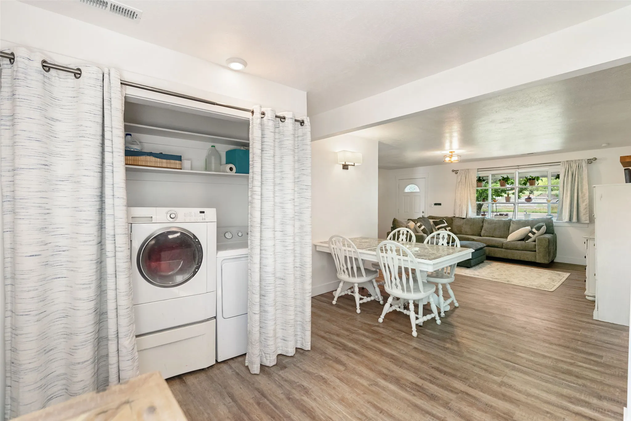 Dedicated laundry closet featuring a stackable washer and dryer, adjacent to a dining area with wood-finish flooring