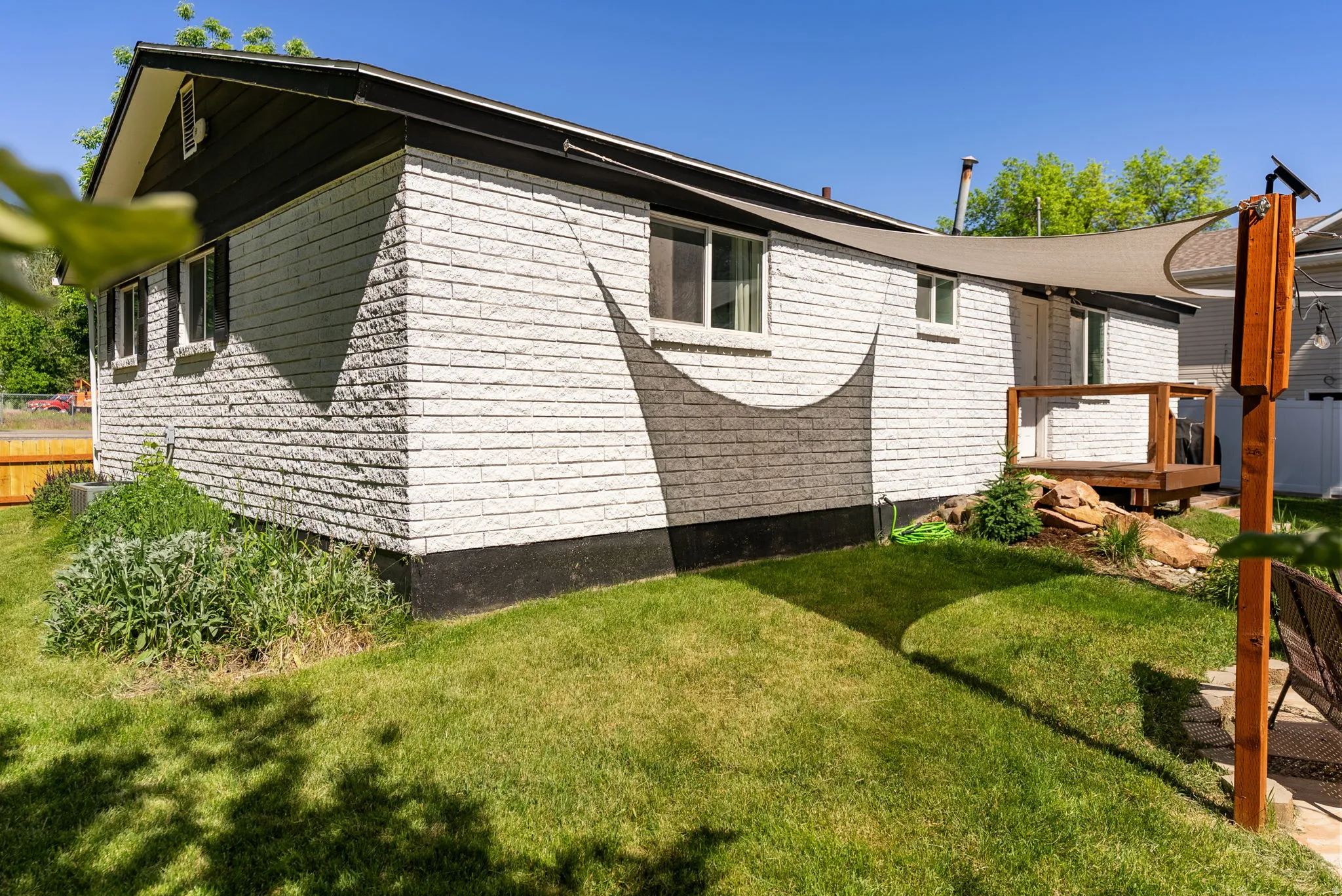 Exterior featuring white painted brick, dark trim, a wooden deck, and a sloped lawn with landscaping