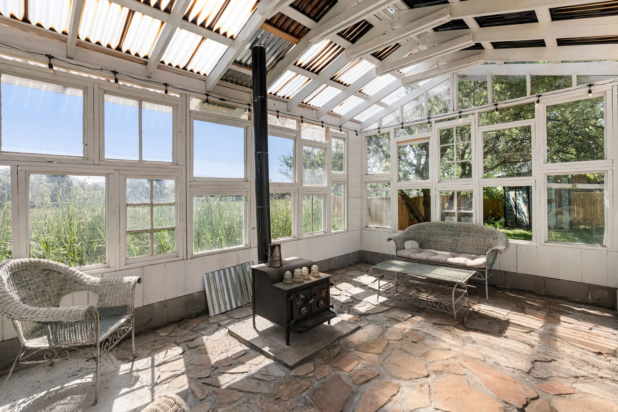 Sunroom featuring a wood-burning stove with a stovepipe, flagstone flooring, multiple pane windows, and a clear corrugated roof