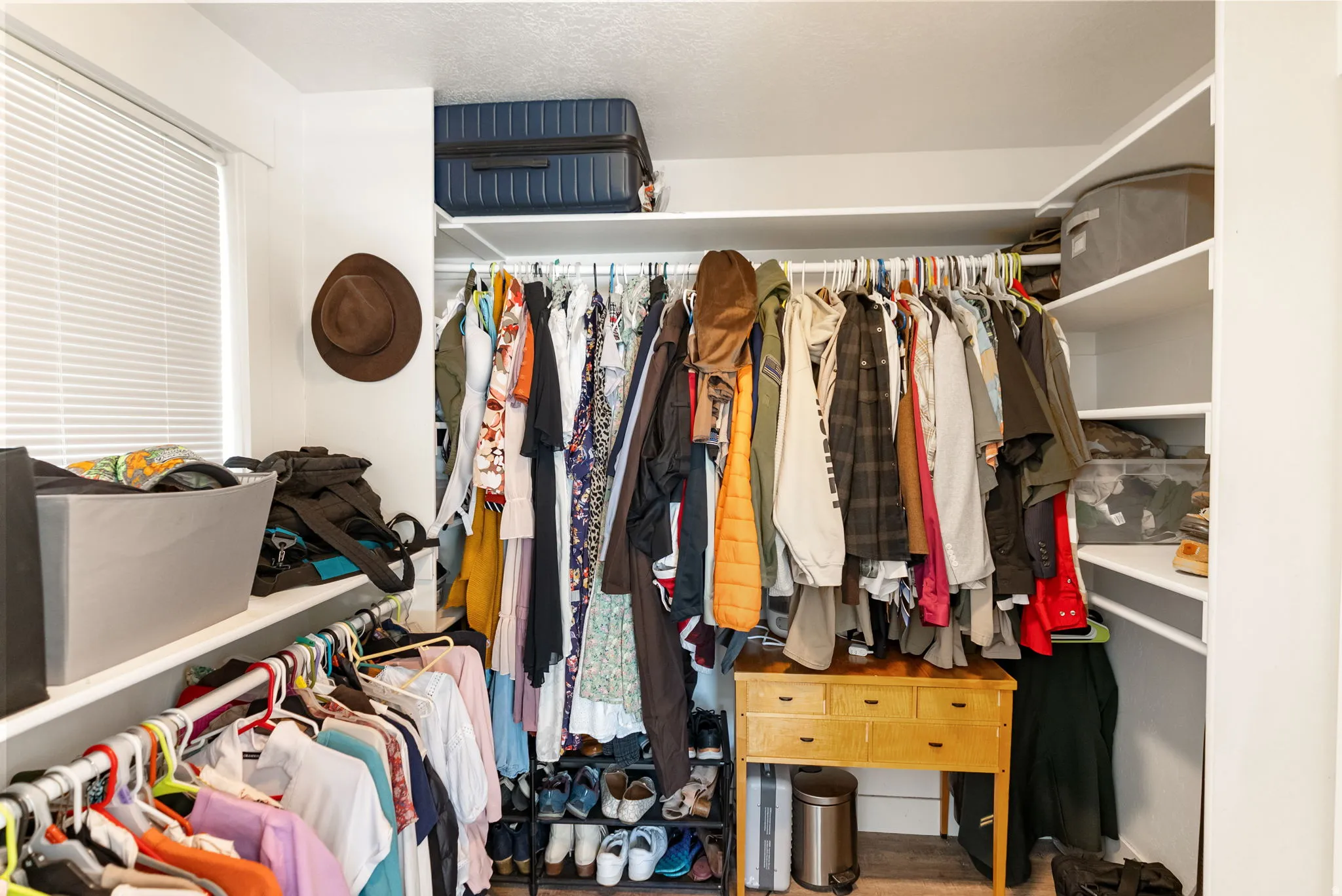 Walk-in closet featuring built-in shelving, multiple hanging rods, a window with blinds, and white walls
