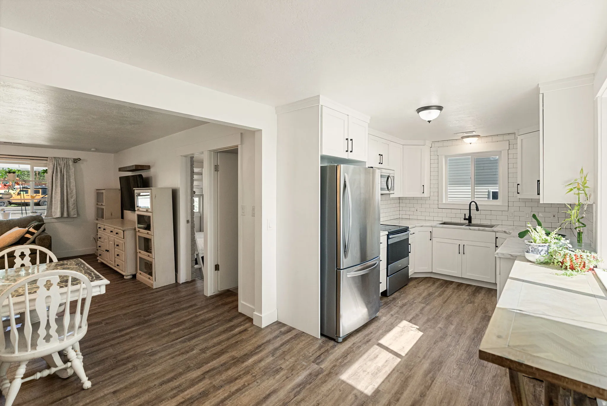 Modern kitchen featuring white shaker cabinetry, stainless steel appliances, a white subway tile backsplash, and wood-finish flooring
