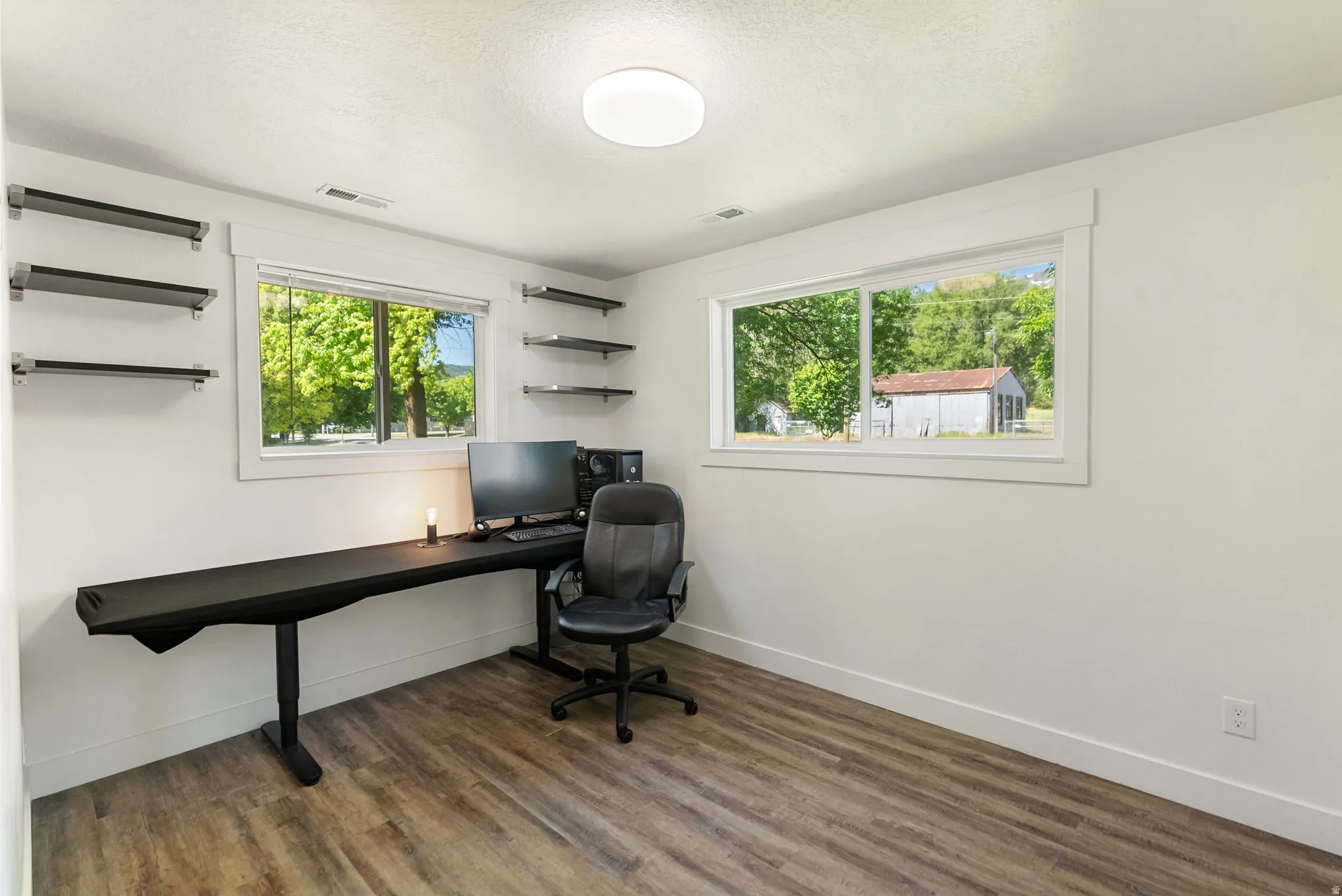 Spacious room with wood-finish flooring and multiple windows providing natural illumination