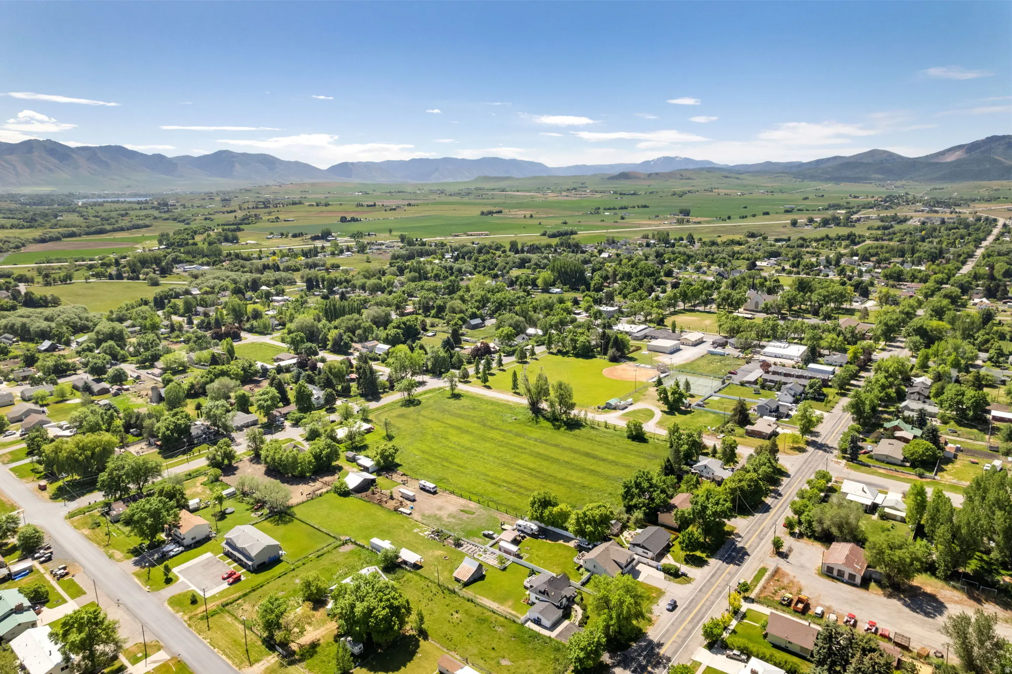 Expansive aerial view of a verdant rural landscape featuring a residential community, agricultural fields, and distant mountains