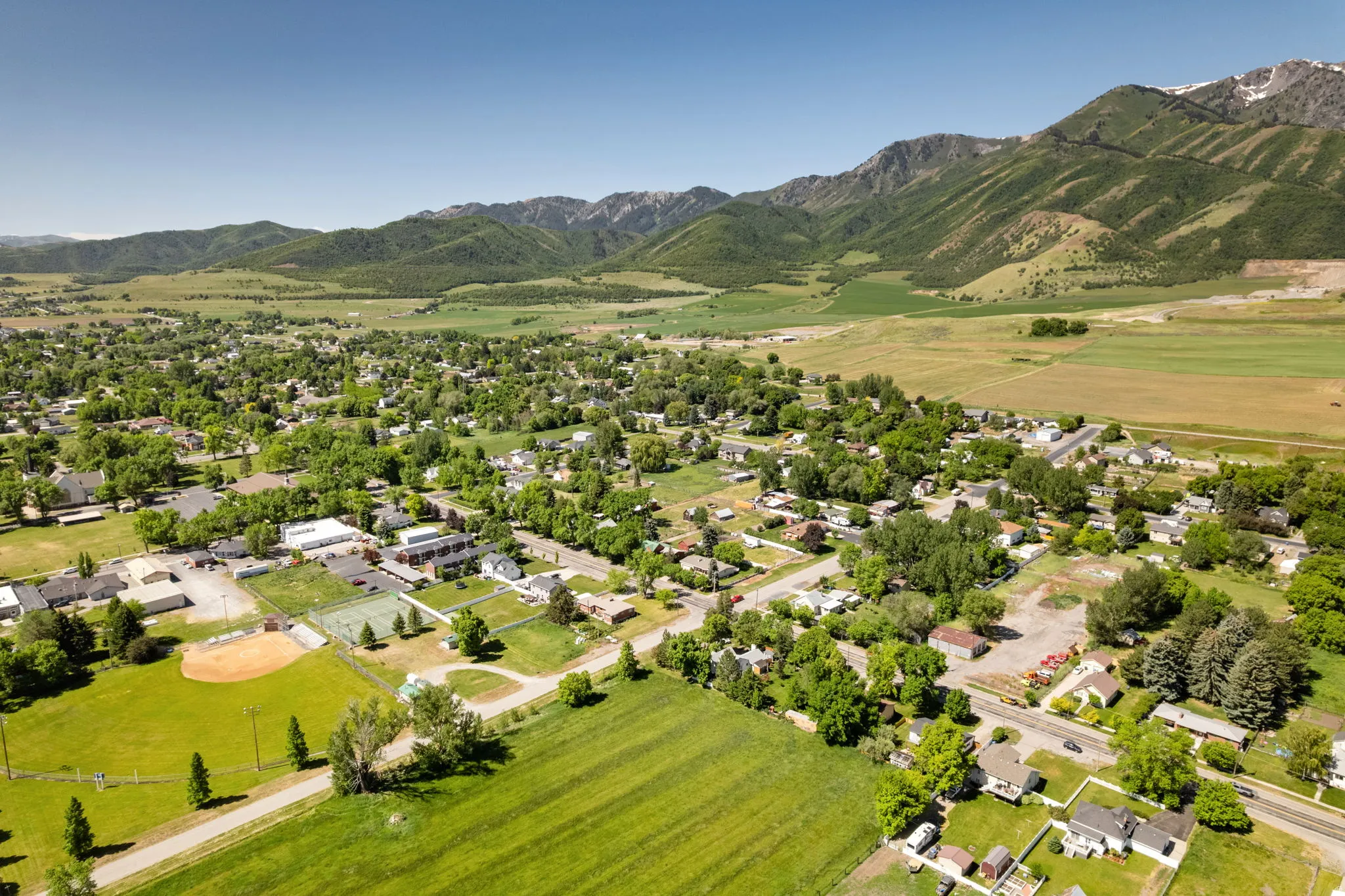 Expansive aerial perspective showcasing a residential community nestled within a verdant valley, framed by majestic mountains with visible snowcaps
