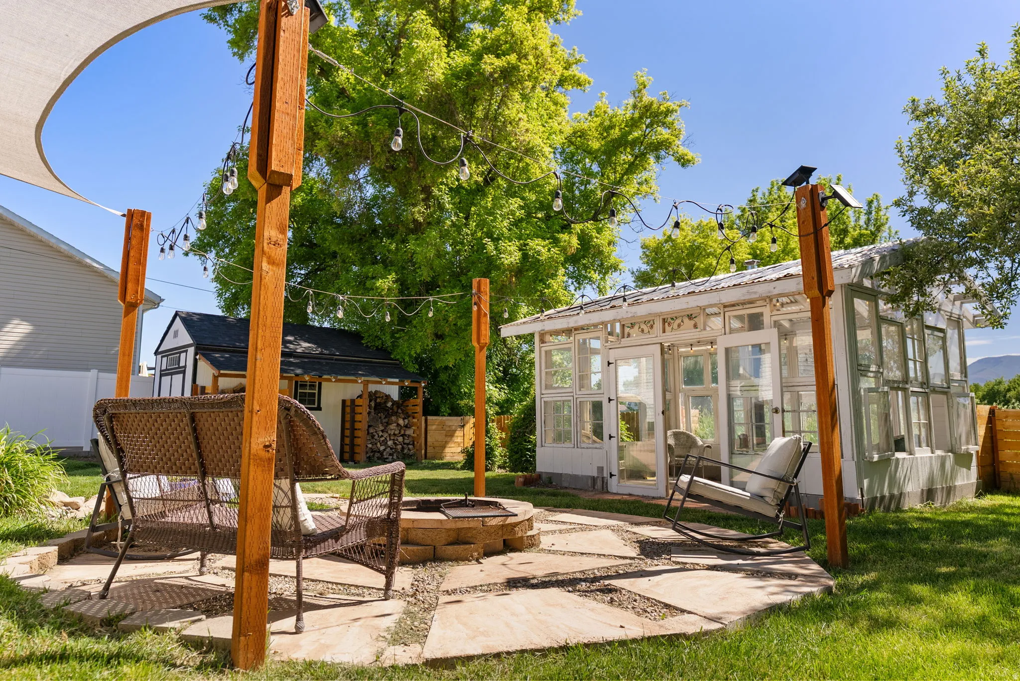 Outdoor living space featuring a stone fire pit, string lighting, and a shade sail