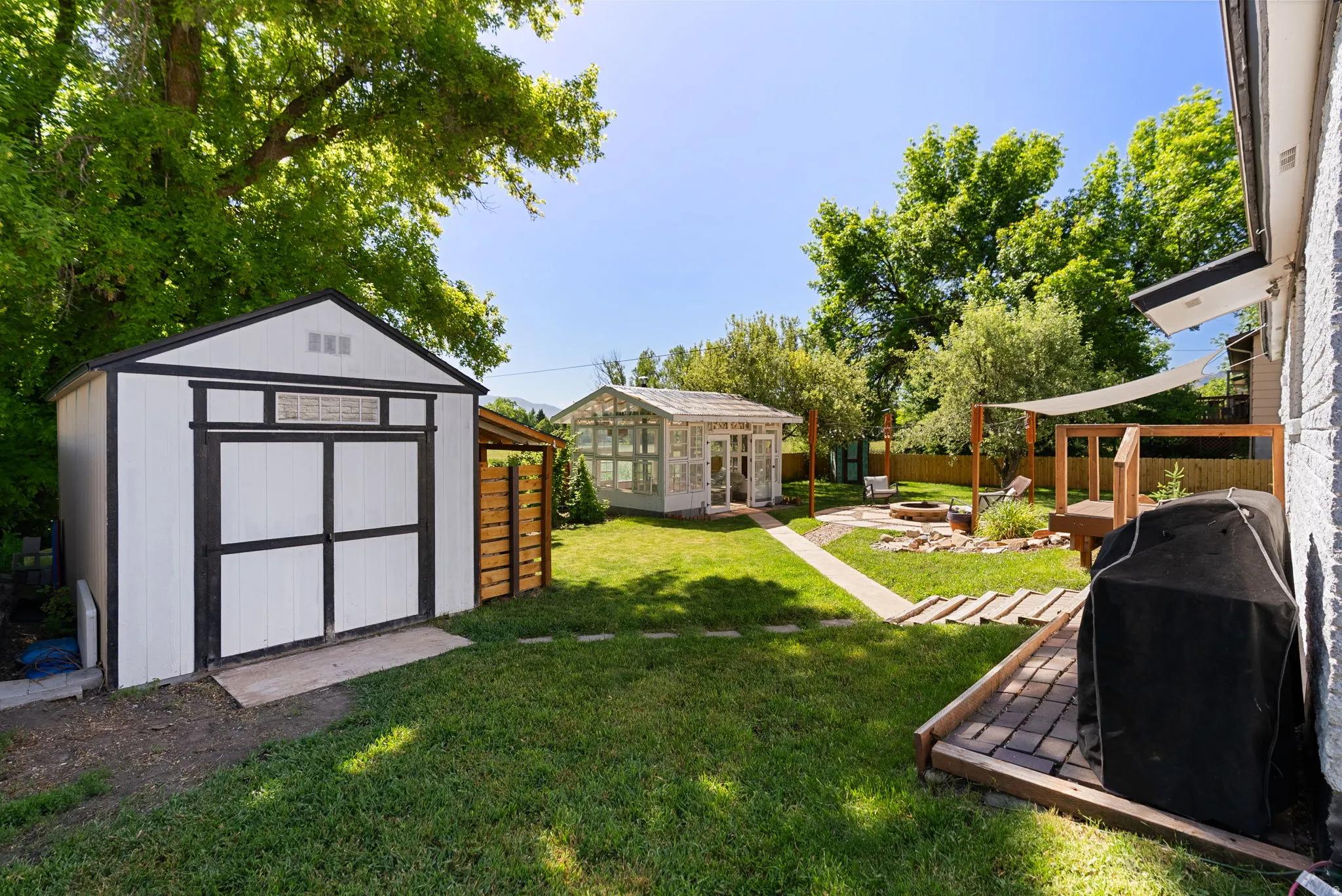 Spacious backyard featuring a dedicated storage shed, a charming greenhouse structure, a paver patio, and a fire pit area