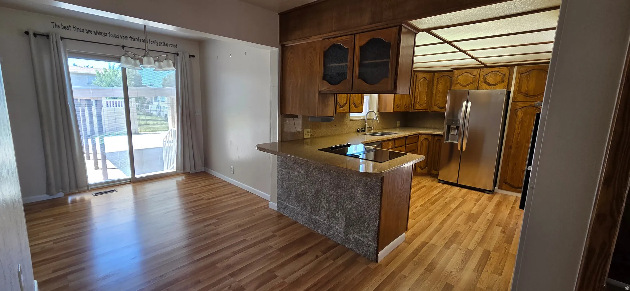 Open-concept kitchen and dining area featuring wood-finish flooring, abundant wood cabinetry, stainless steel appliances, a built-in cooktop, and a sliding glass door providing outdoor access