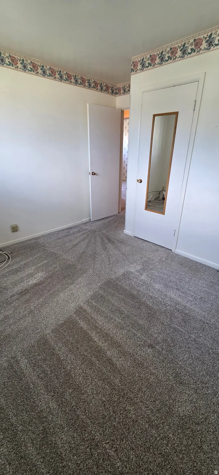 Wall-to-wall carpeting with a light gray hue, white painted walls, and a floral-patterned wallpaper border