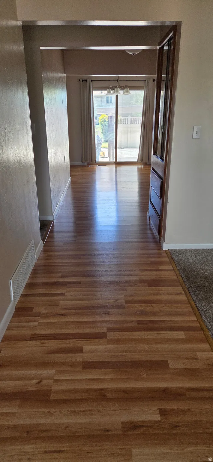 Wood-finish flooring extending from the entryway through to a rear room, featuring sliding glass doors and a view of the outdoor patio
