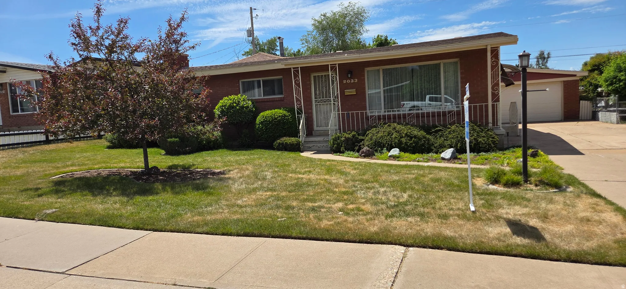 Brick facade ranch-style residence featuring a covered front entry, established front yard landscaping, and an attached garage with an extended driveway