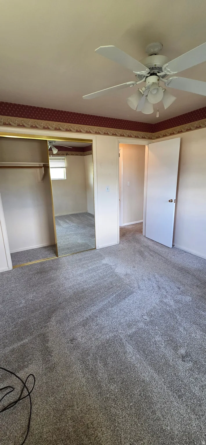 Carpeted room featuring a ceiling fan with integrated lighting, a mirrored closet door, a closet with a built-in rod, and a doorway