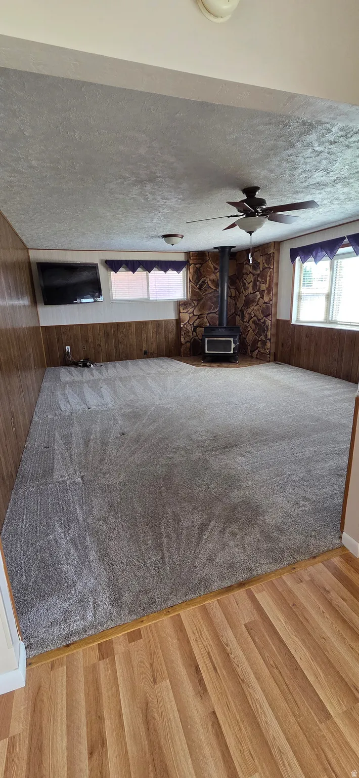 Spacious room featuring gray carpeting, wood-finish wall paneling, and a corner wood-burning stove with a stone surround