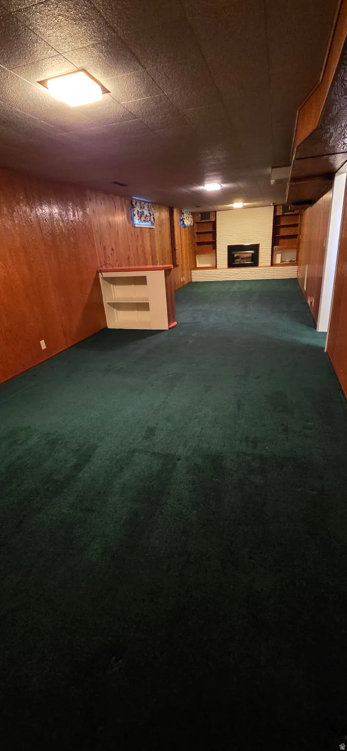 Spacious room featuring green carpeting, wood paneling, a built-in bar, and a fireplace with integrated shelving