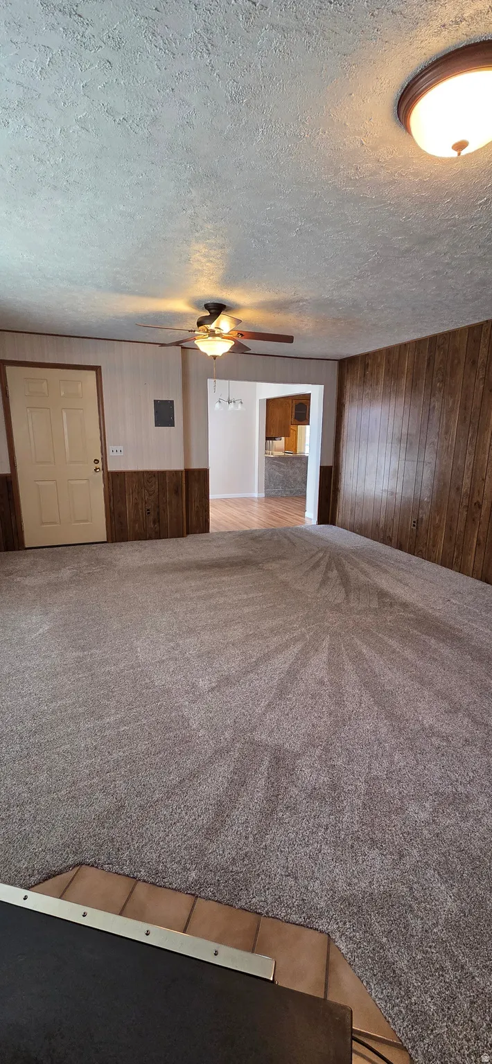 Carpeted living area featuring wood-paneled accent walls and ceiling fan with integrated lighting