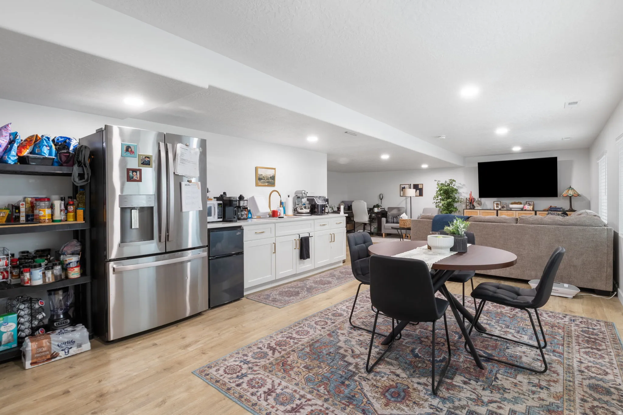 Open-concept space featuring wood-finish flooring, white cabinetry with gold hardware, and recessed lighting