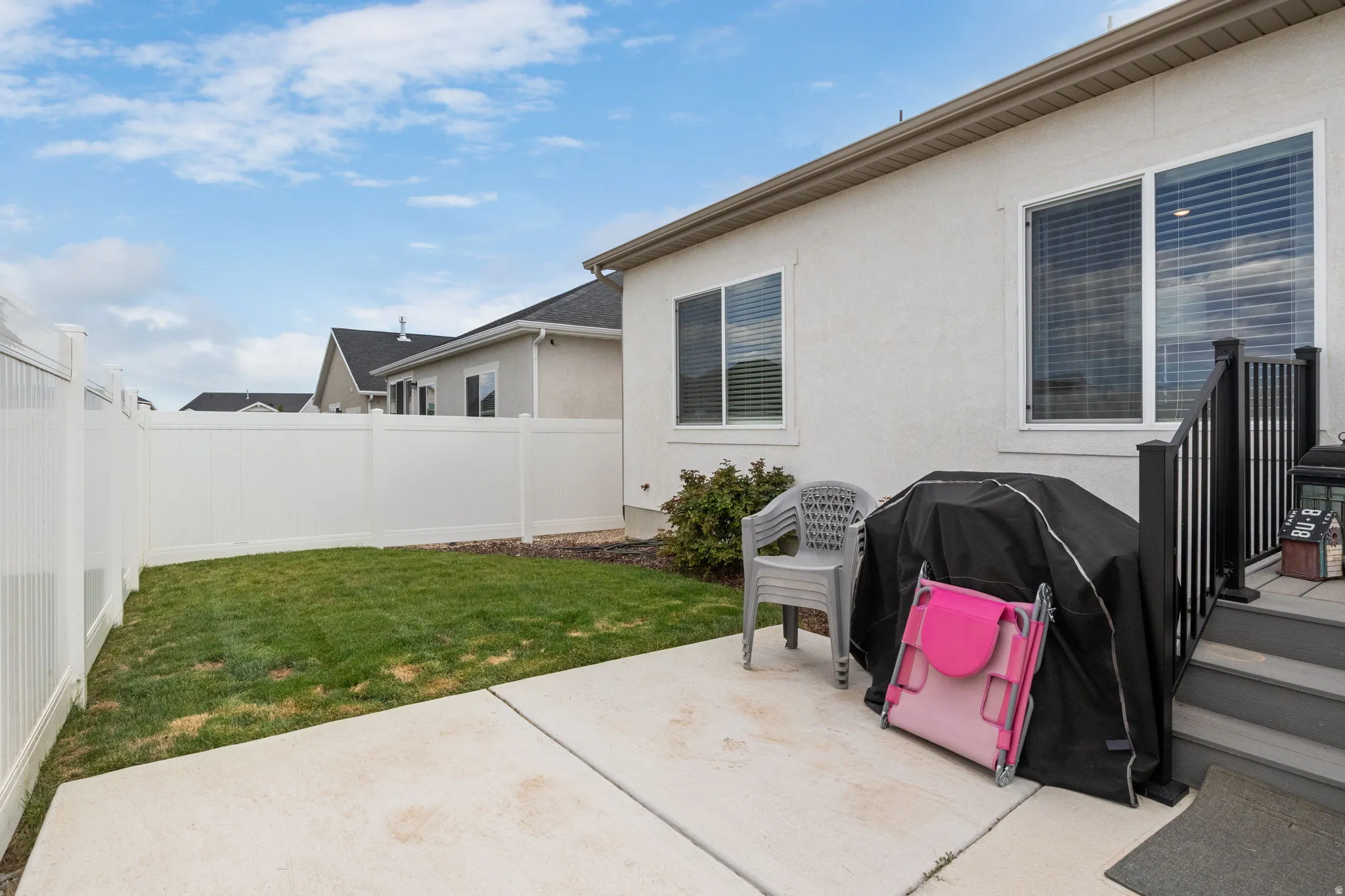 Private backyard featuring a concrete patio, green lawn, and full white vinyl fencing
