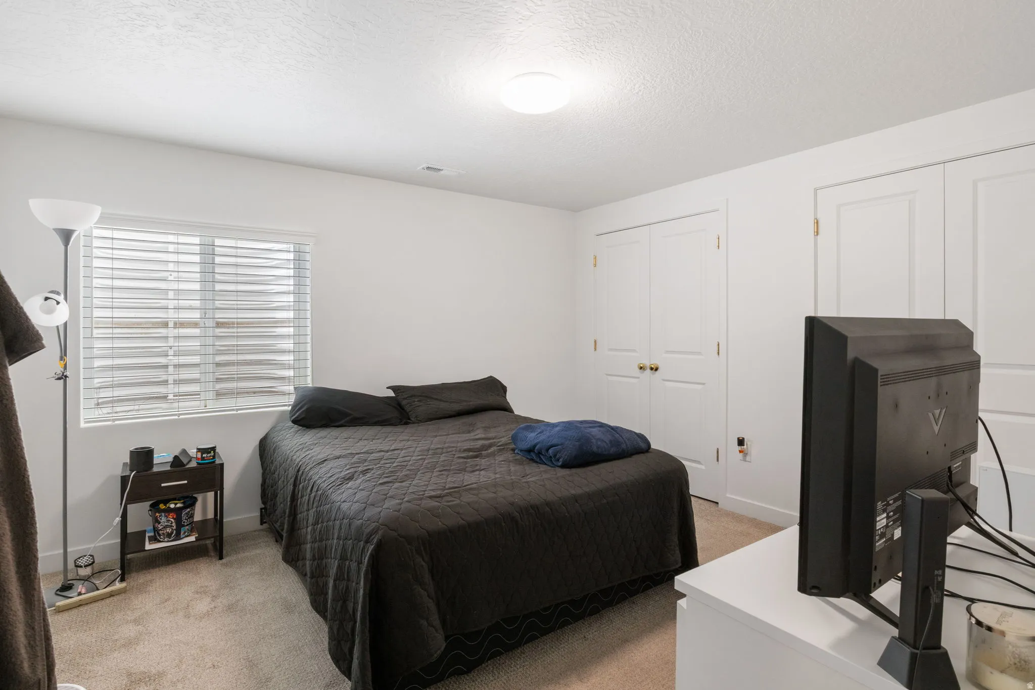 Carpeted room featuring a ceiling-mounted light fixture, a window with horizontal blinds, and multiple bi-fold doors with brass-finish hardware