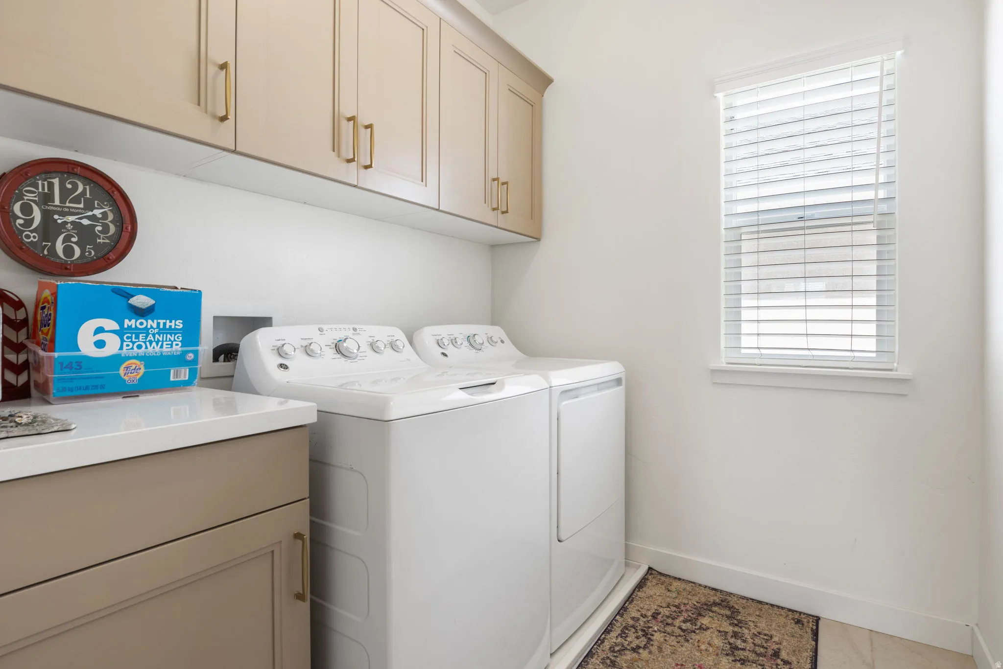 Dedicated laundry room featuring upper and lower cabinetry with gold-tone hardware, a light-toned countertop, and a window with blinds