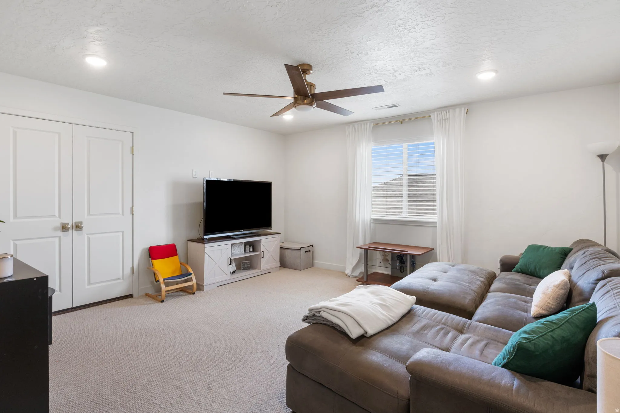 Carpeted living space featuring recessed lighting, a ceiling fan, and window with blinds