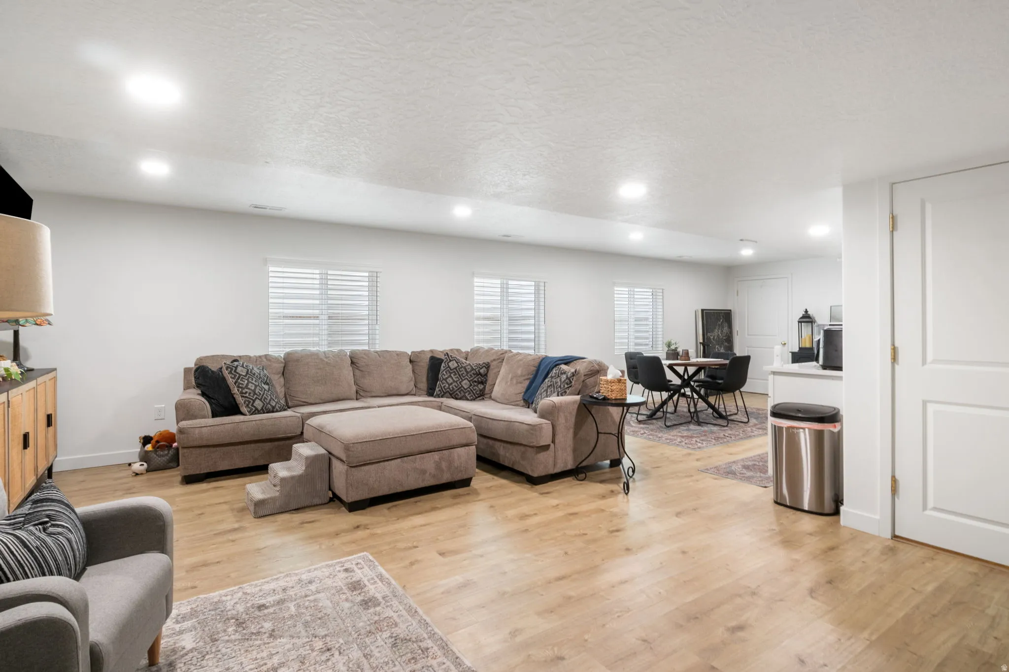 Open-concept living area featuring wood-finish flooring, recessed lighting, and multiple windows with horizontal blinds