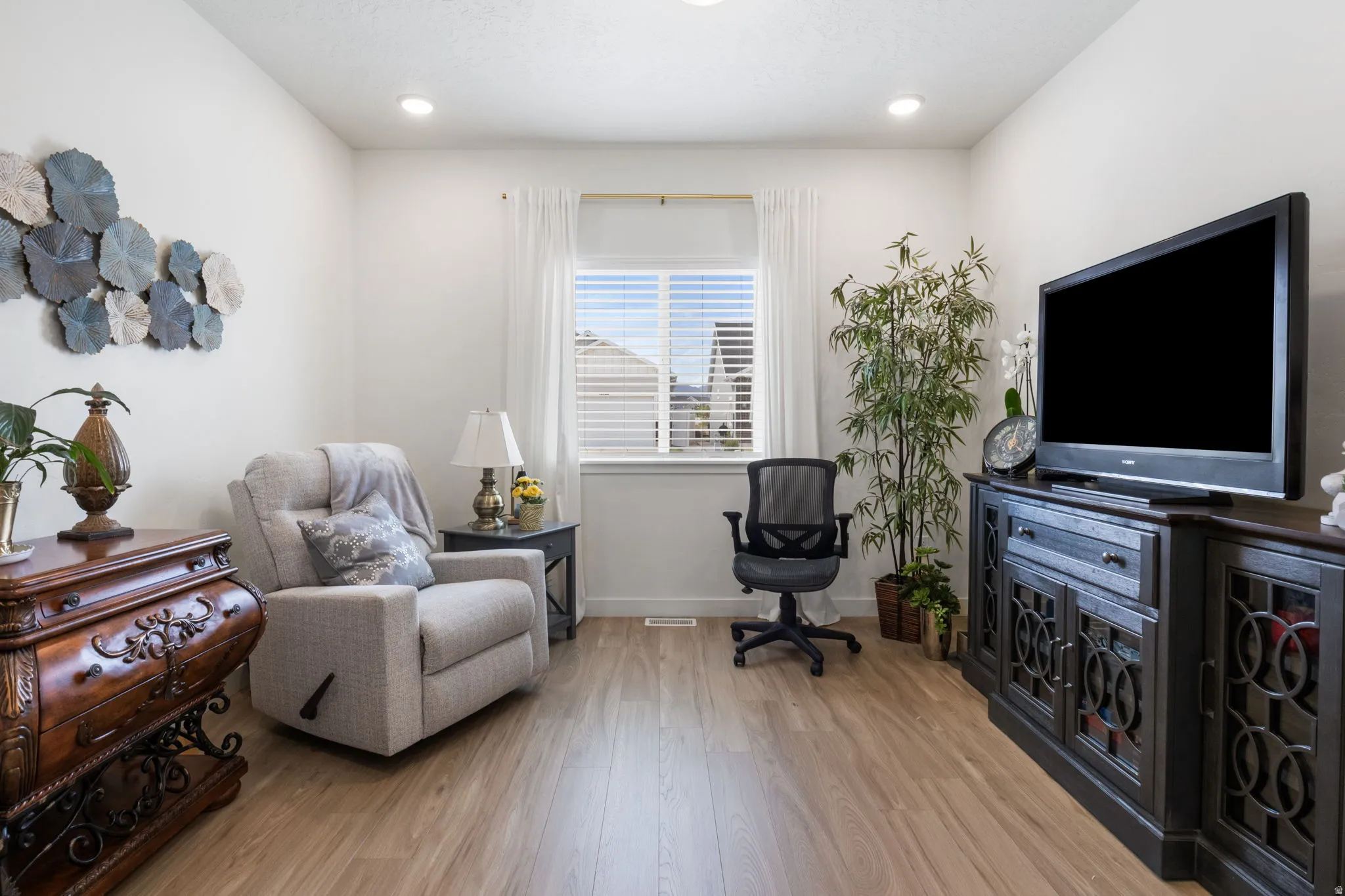 Living area featuring wood-finish flooring, recessed lighting, and a window with blinds and sheer curtains