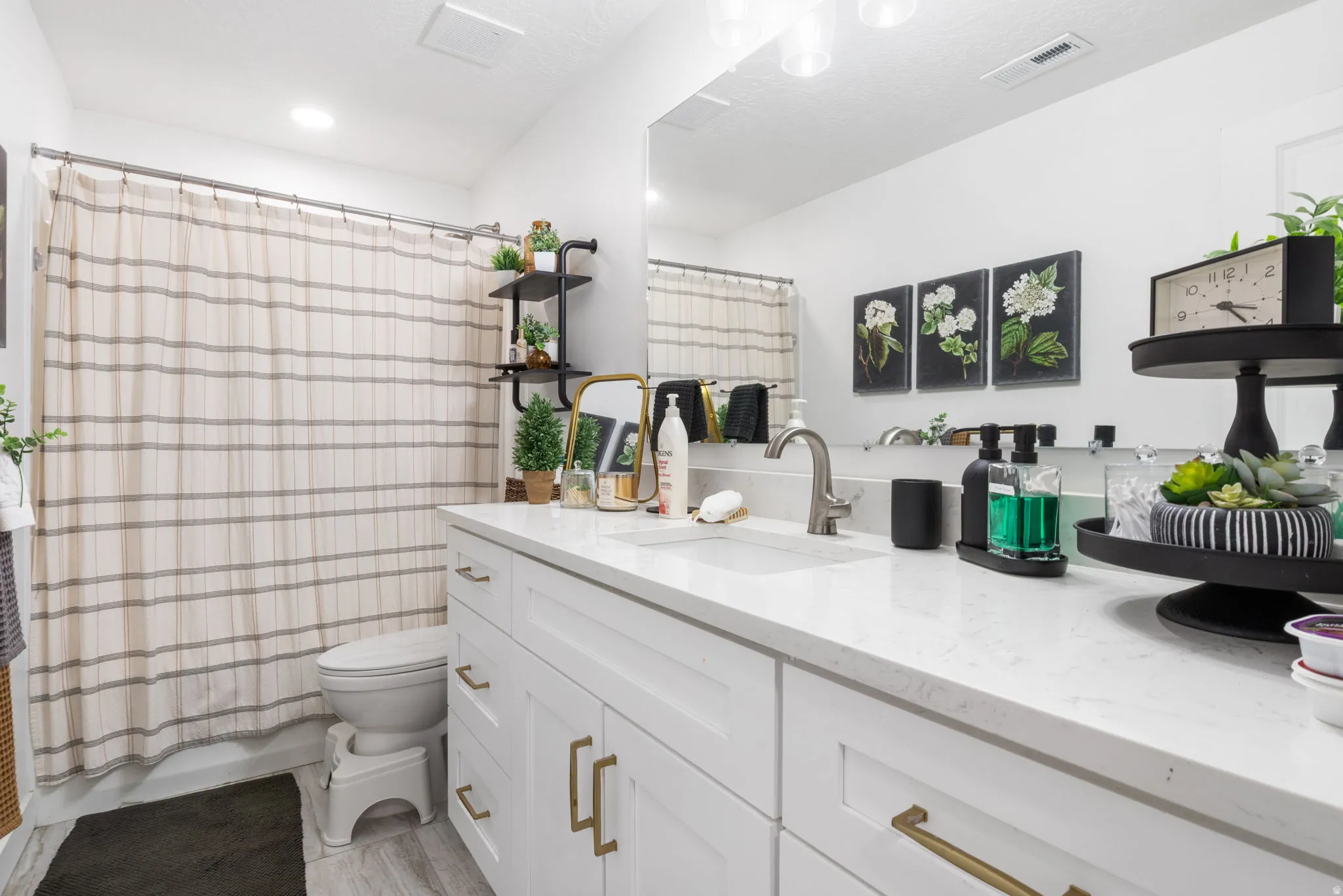 Spacious bathroom featuring a white vanity with gold-finish hardware, a single basin sink, and a stone-finish countertop