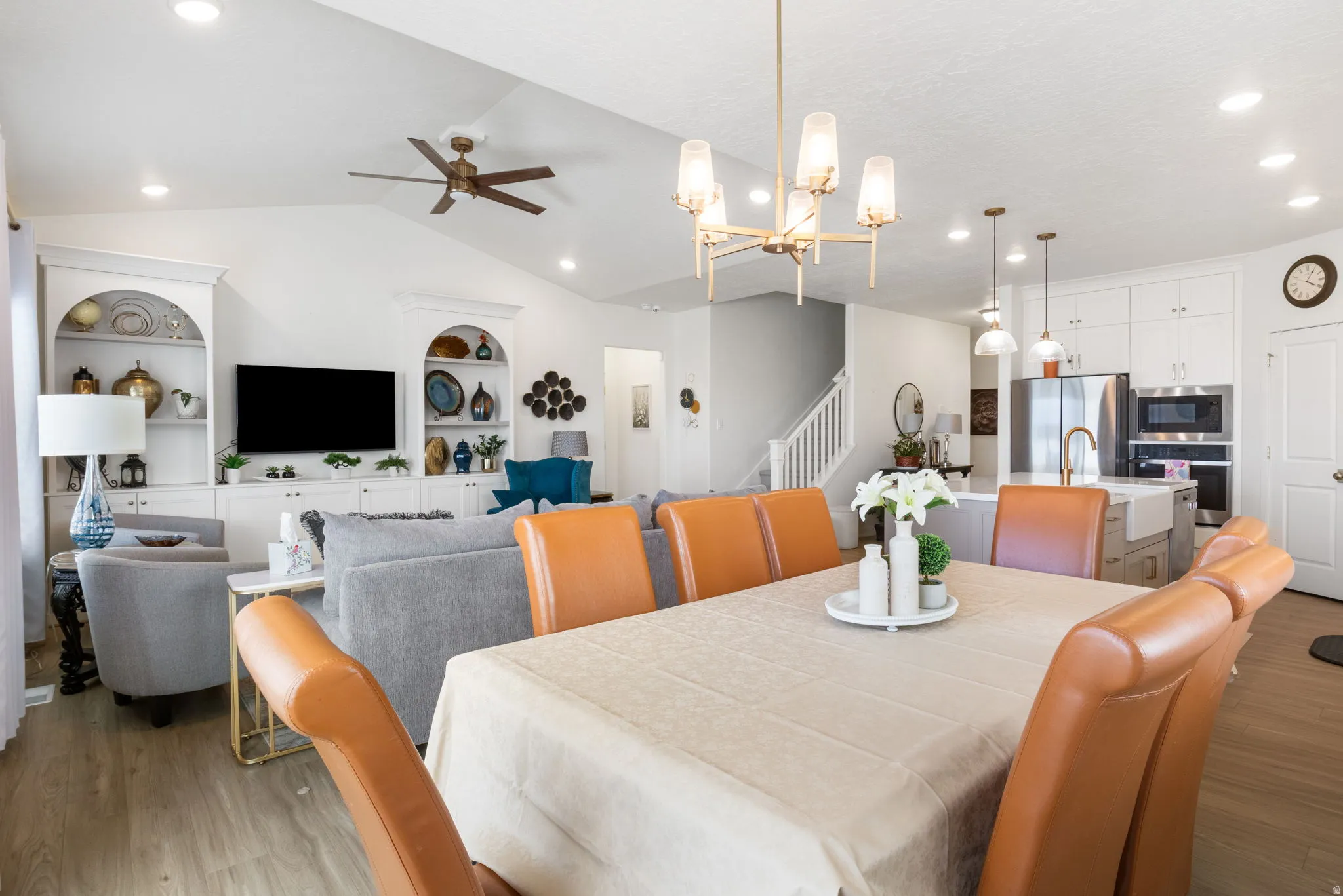 Open-concept living space featuring wood-finish flooring, vaulted ceilings with recessed lighting, a modern chandelier, and built-in cabinetry with arched display shelves