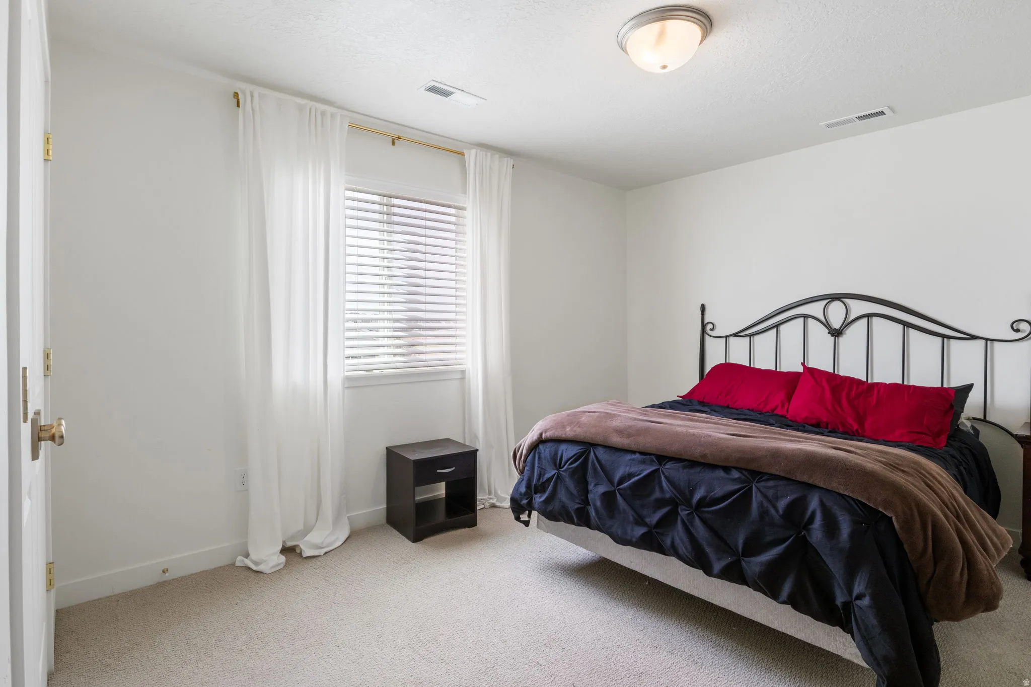 Bright room featuring a window with horizontal blinds and full-length sheer curtains
