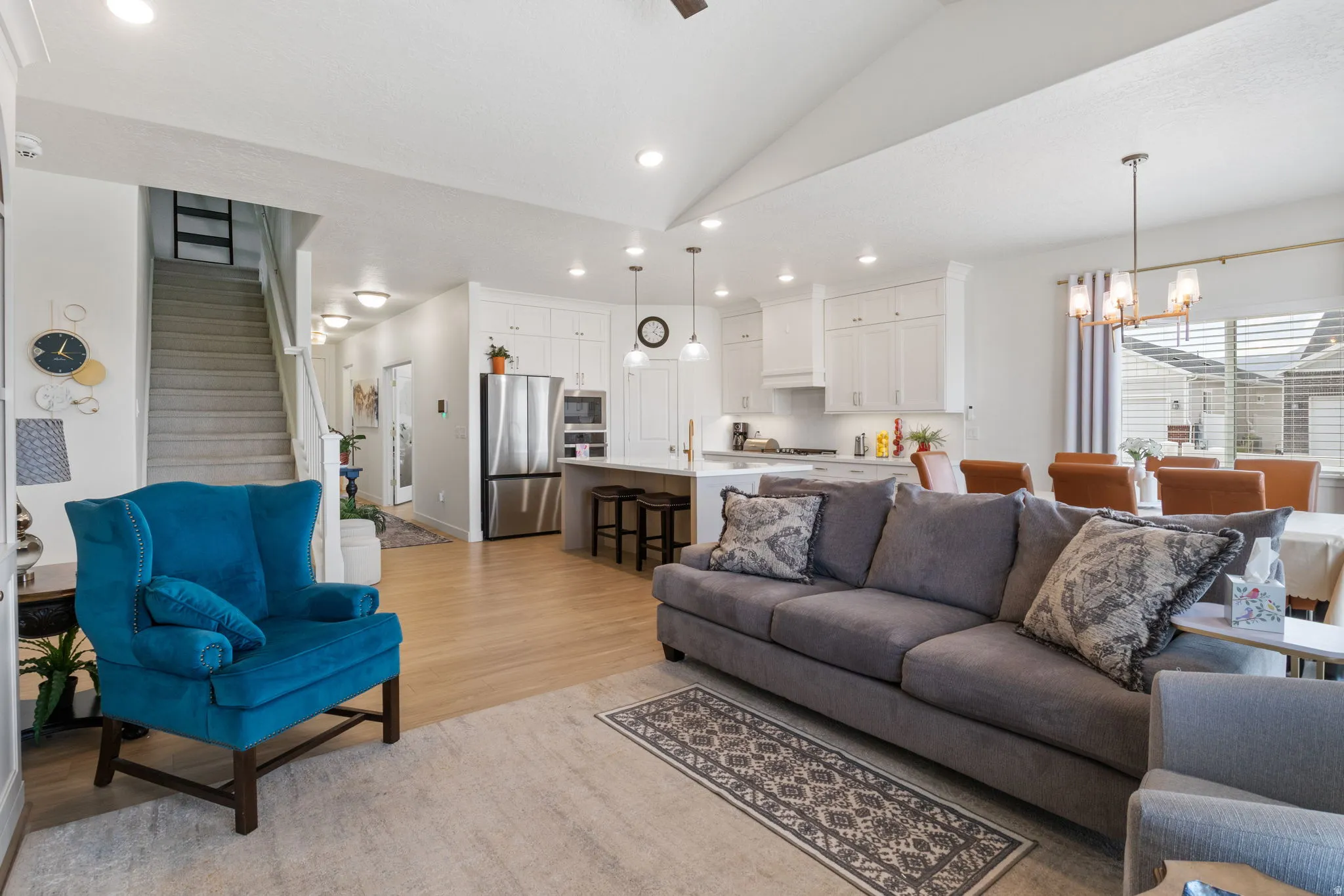 Open-concept living space featuring vaulted ceilings, light wood-finish flooring, a contemporary kitchen with white cabinetry and stainless steel appliances, and a dining area with a modern chandelier