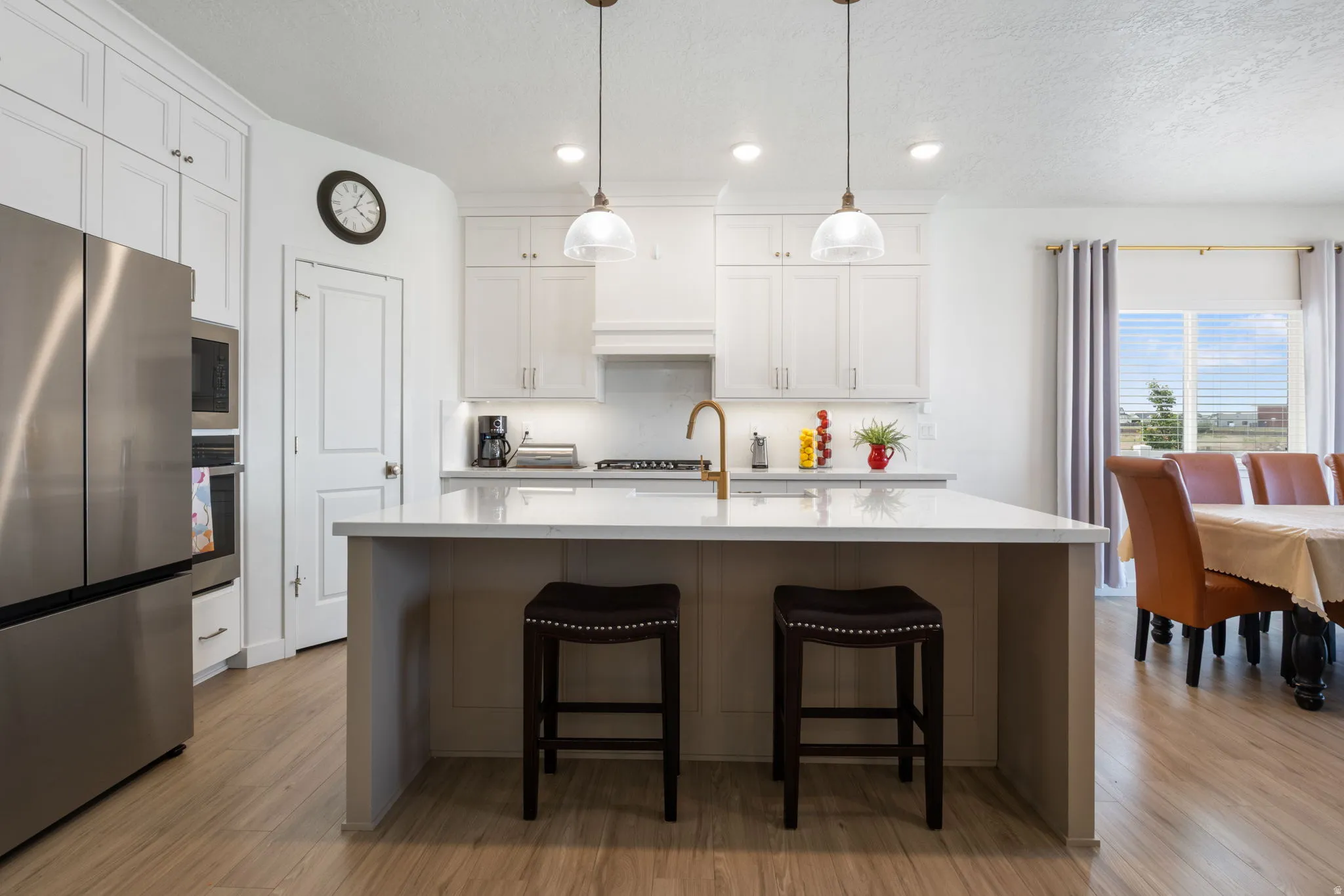 Modern kitchen featuring white cabinetry, stainless steel appliances, a center island with countertop seating, wood-finish flooring, and pendant lighting