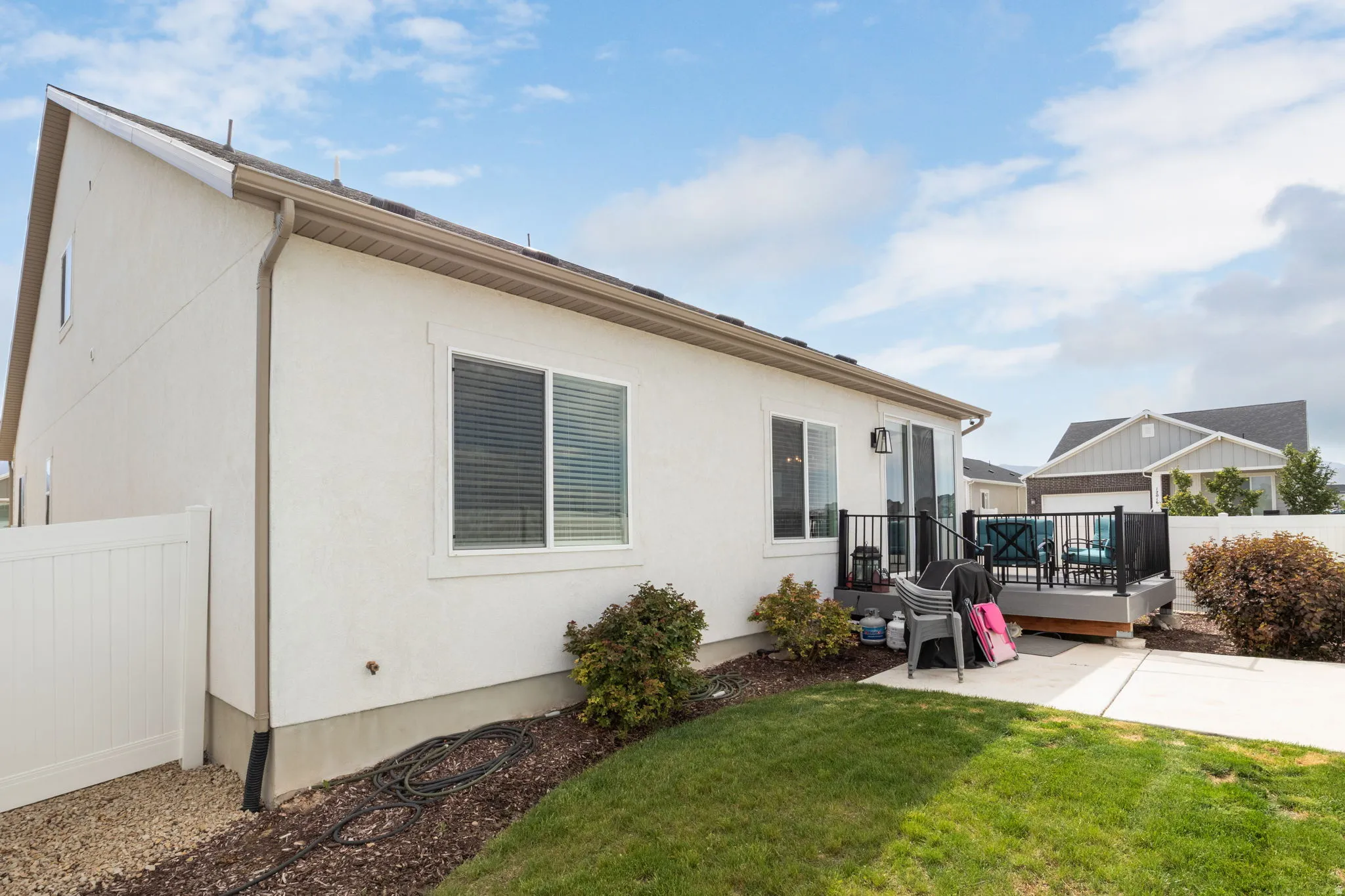 White stucco exterior featuring a rear deck with black railings, a sliding glass door, a privacy fence, and a concrete patio