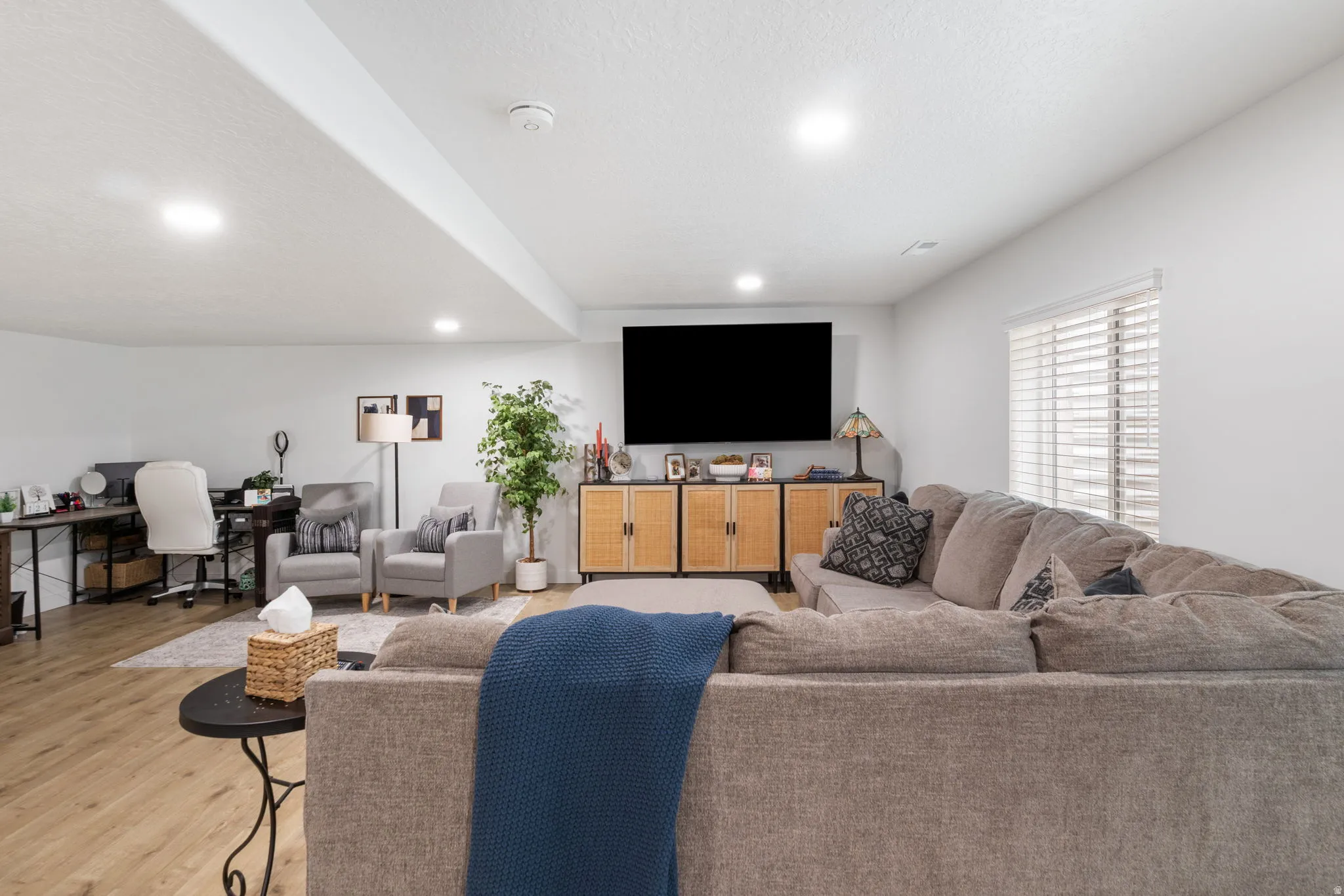 Open-concept living area featuring light wood-finish flooring, recessed lighting, white walls, and a window with blinds