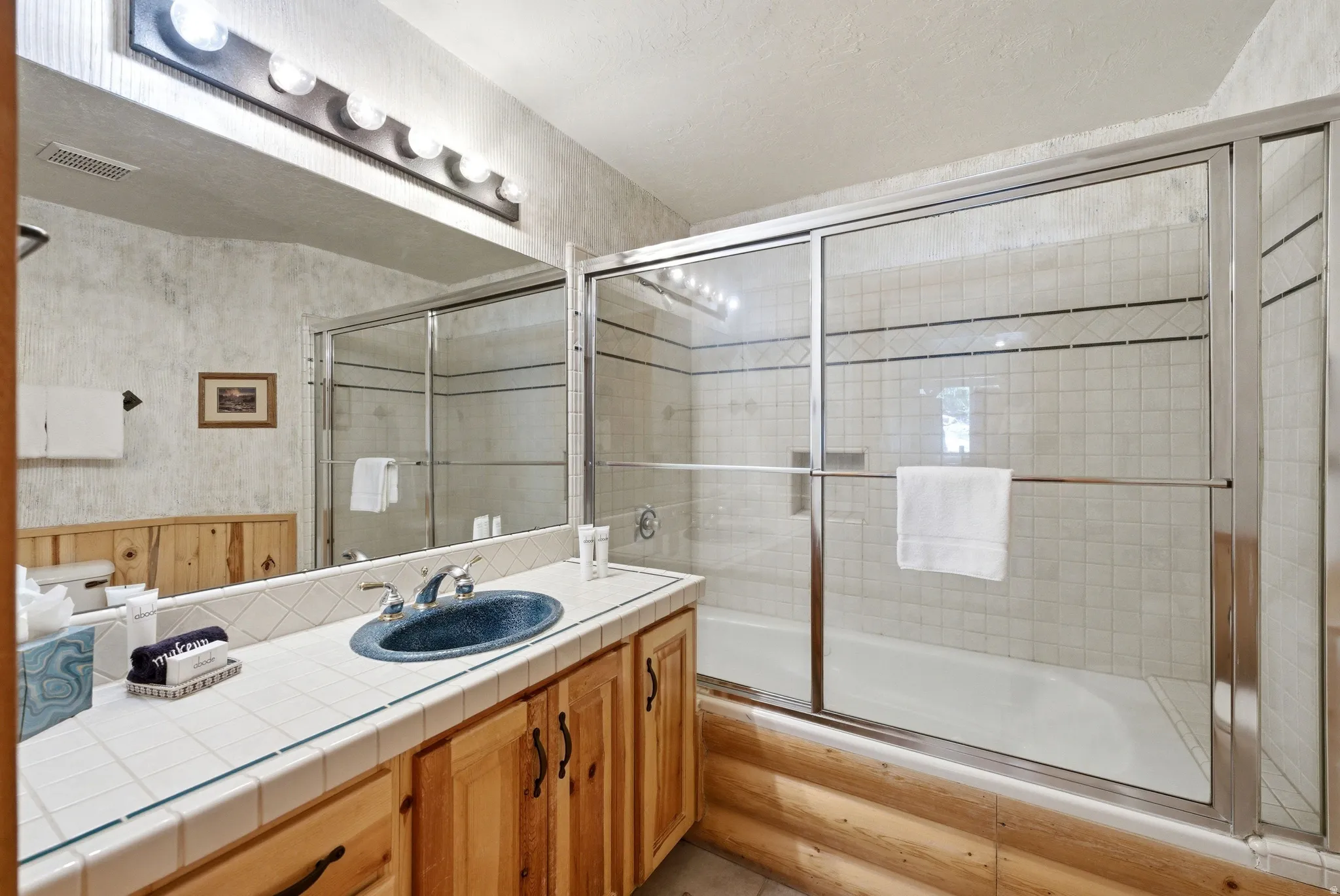 Bathroom featuring a vanity with a blue basin sink, tile countertop, and wood-finish cabinetry