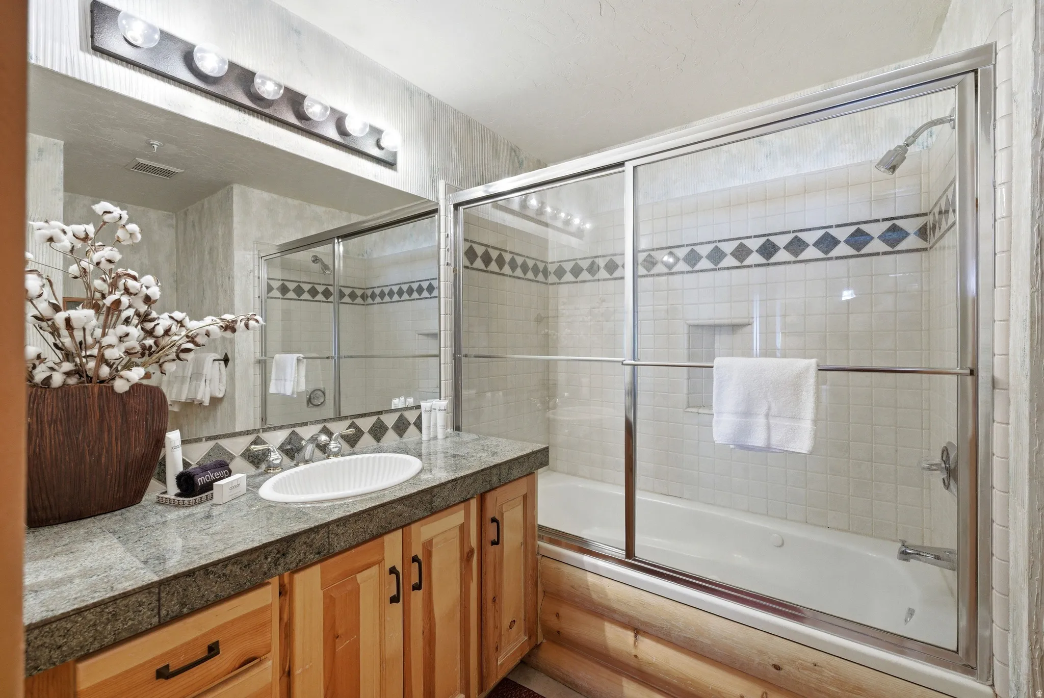 Bathroom featuring a built-in tub with sliding glass shower doors, a vanity with a light-colored countertop, and natural wood cabinetry