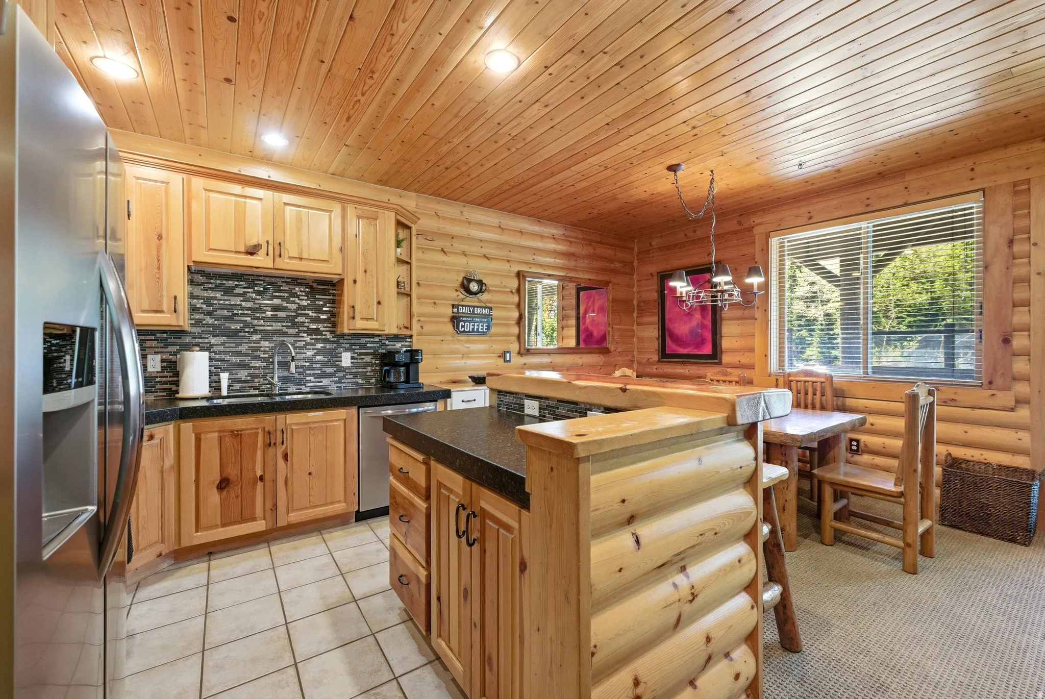 Kitchen featuring a stainless steel refrigerator, dark countertops, tiled backsplash, wooden cabinetry, and tiled flooring
